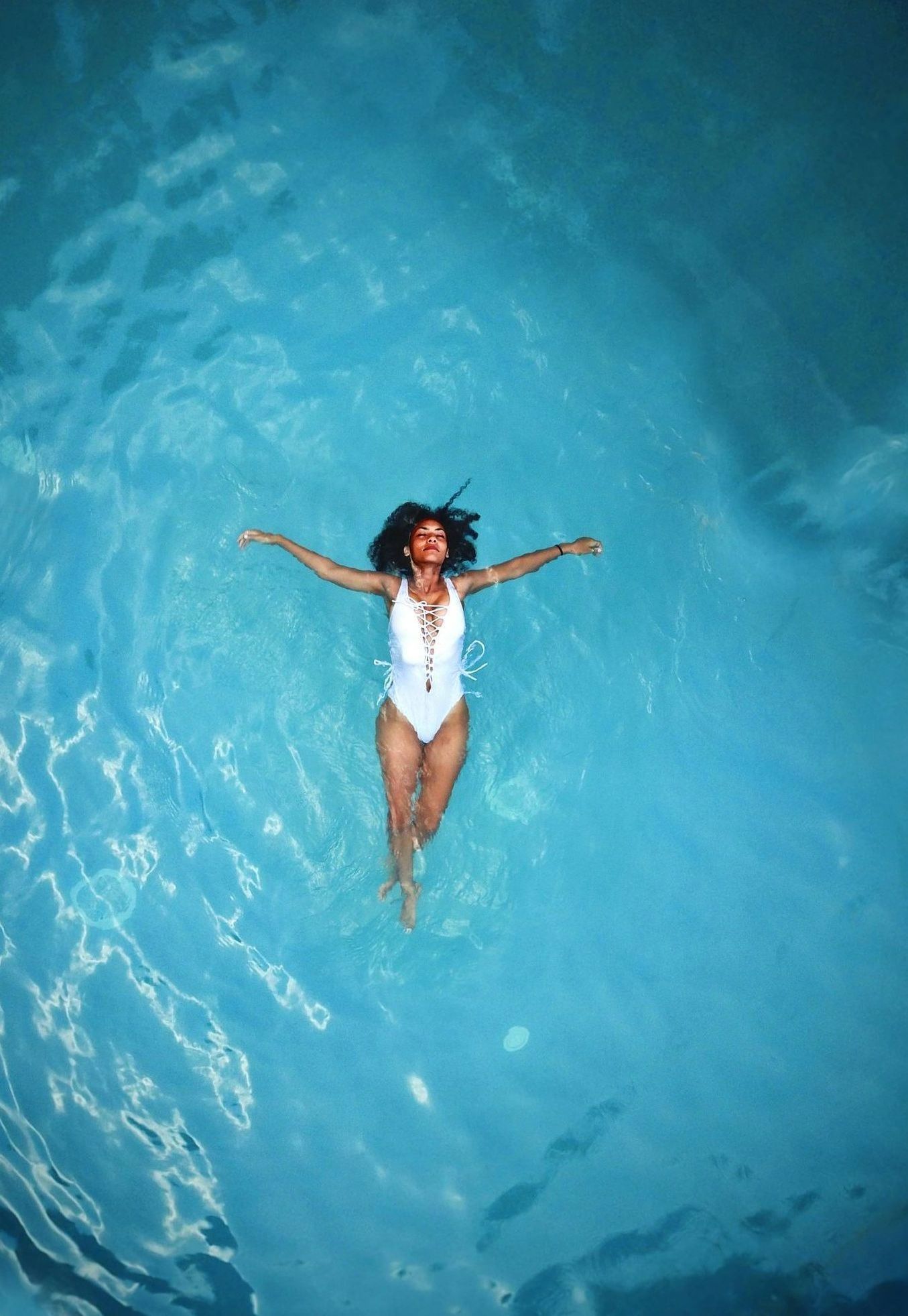 A woman in a white swimsuit is floating in a swimming pool.