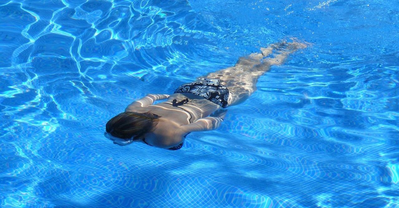 A woman is swimming underwater in a swimming pool.