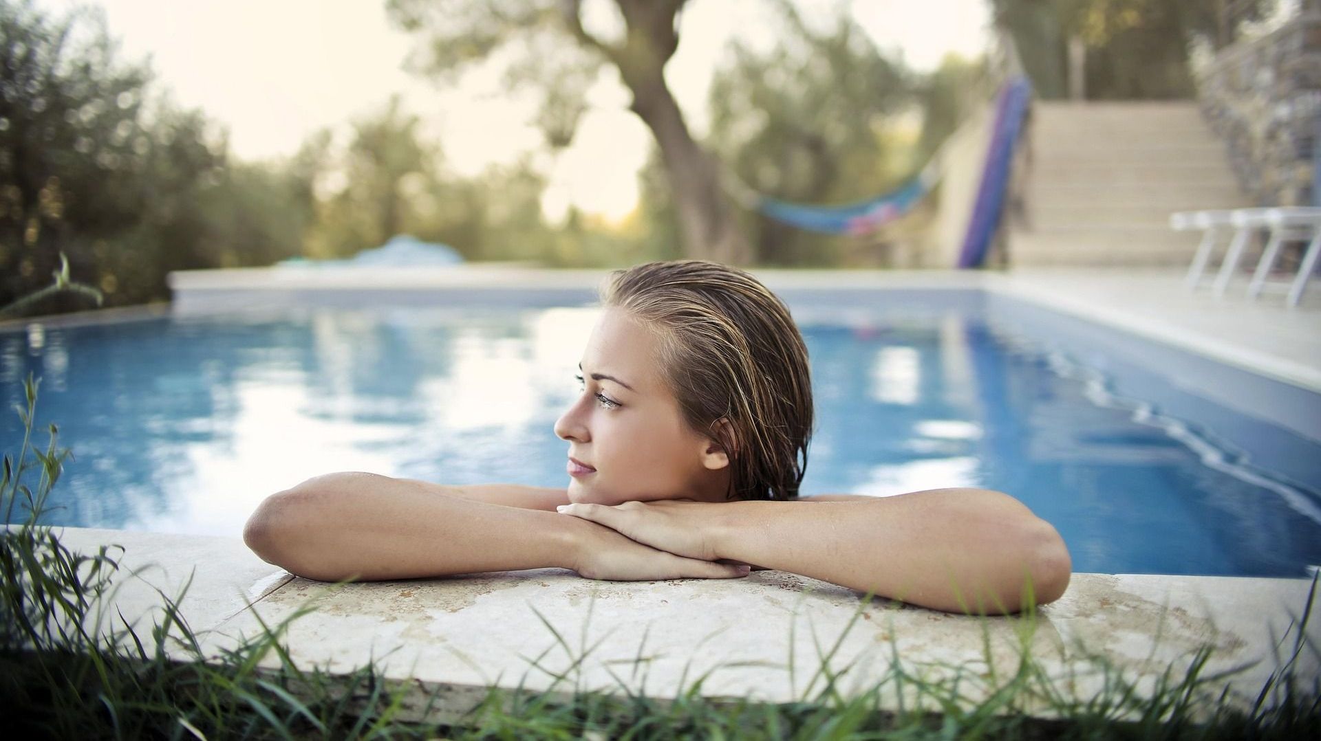 A woman is leaning on the edge of a swimming pool.