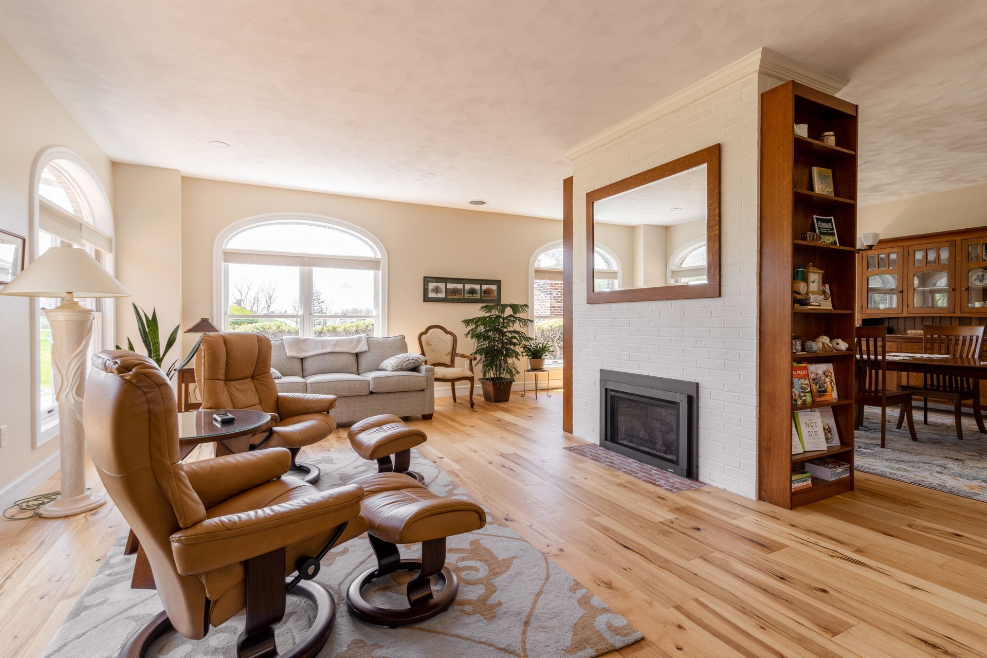 Living room with leather recliner, fireplace, wood floor, and large arched windows.