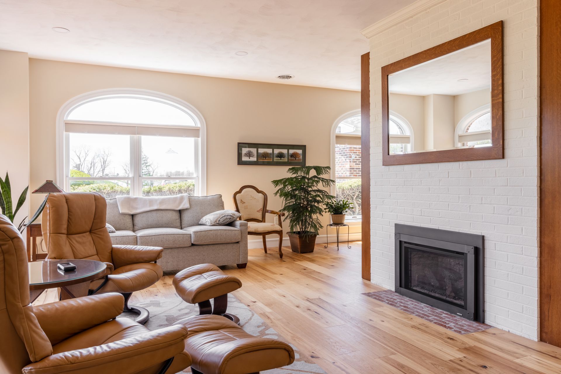 Living room with a fireplace, arched windows, light-colored walls, hardwood floors, and comfortable furniture.