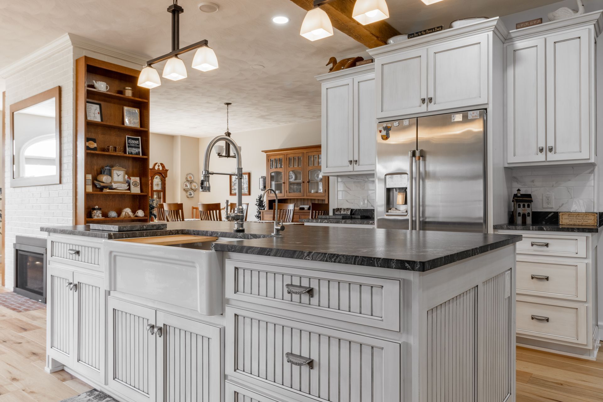 White kitchen with island, stainless steel fridge, wooden cabinets, and dark countertop.
