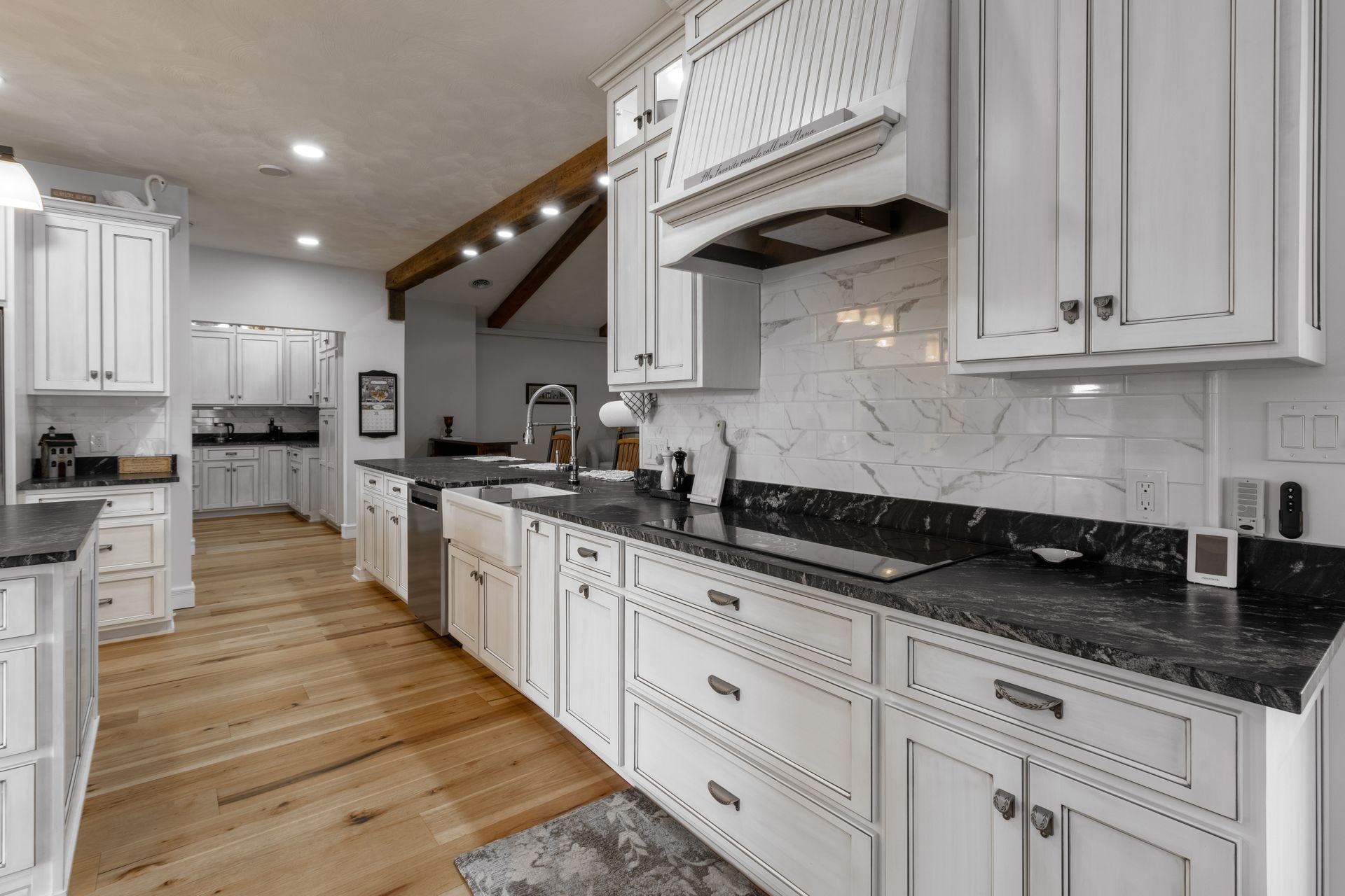 White kitchen with black countertops, light wood floors, and stainless steel appliances.