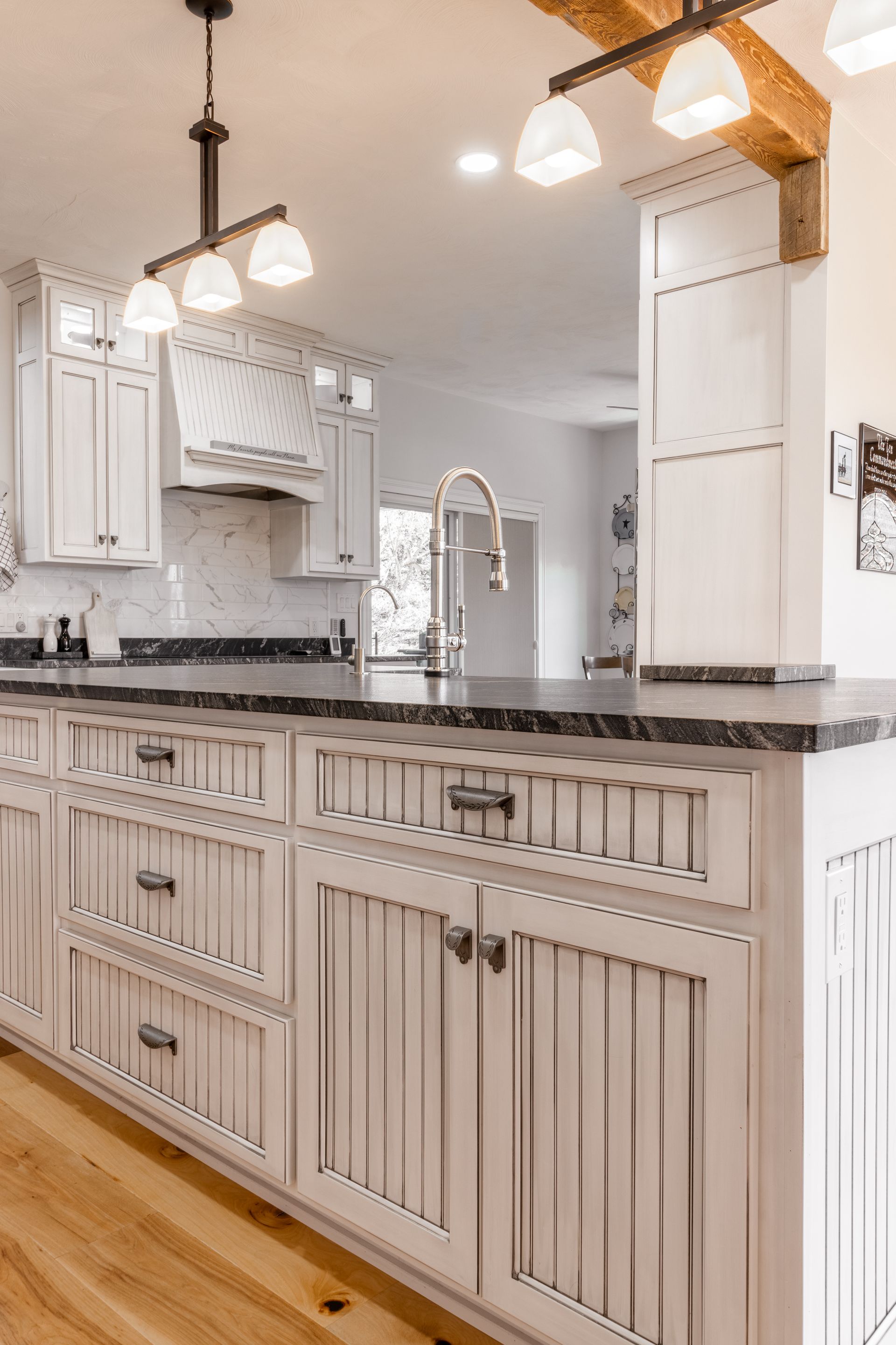 White kitchen island with cabinets, drawers, and dark countertop. Wooden beams, light fixtures, and white cabinetry.
