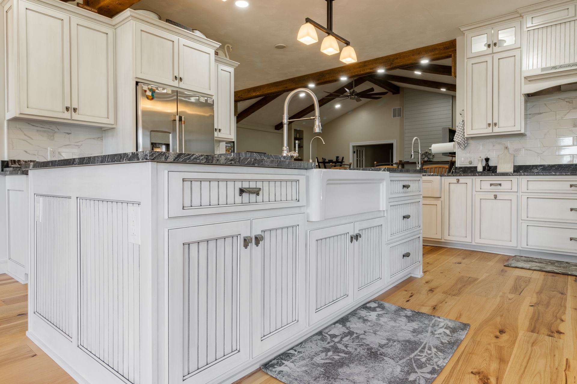 White kitchen with large island, stainless steel appliances, and wooden floors.