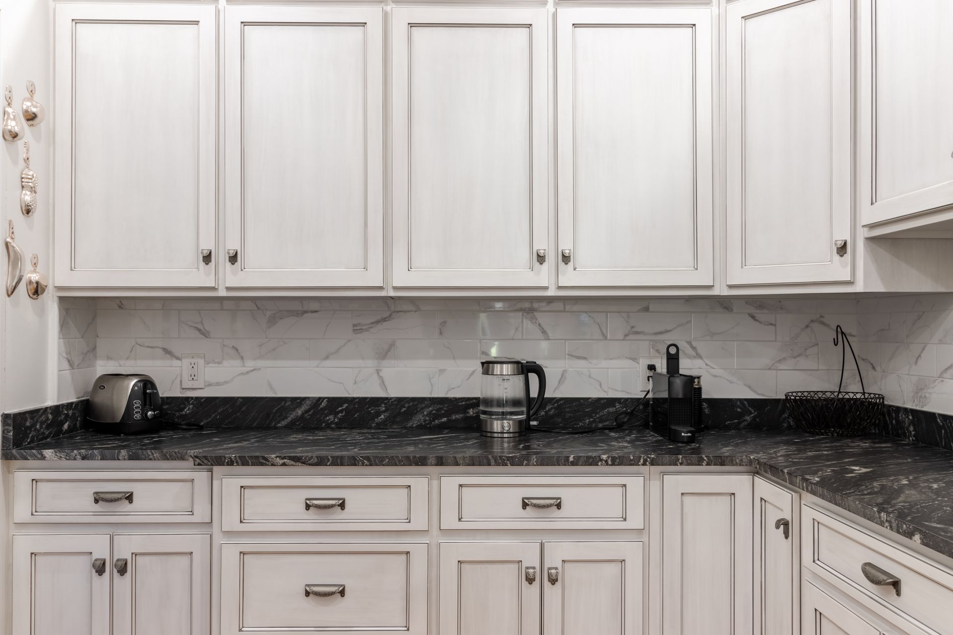 White kitchen cabinets with black countertops, a backsplash, and appliances.