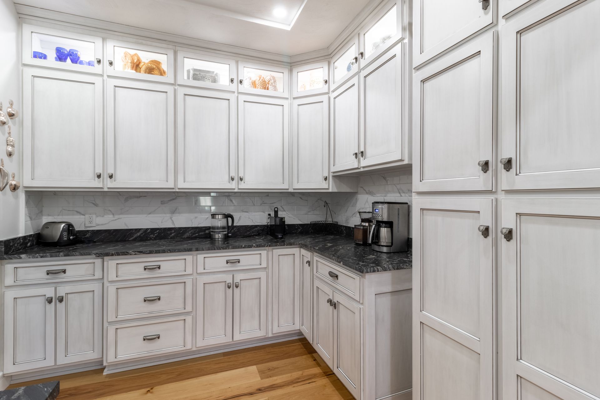 White kitchen cabinets with black countertops and wood floor.