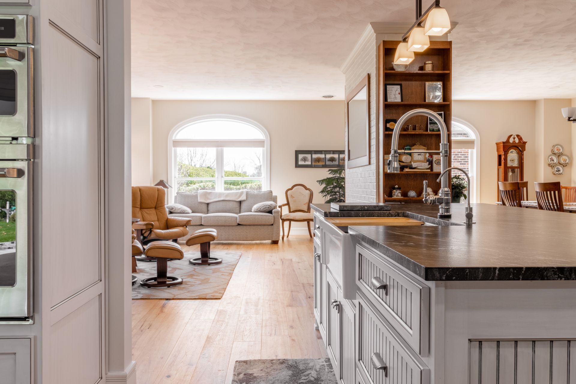 Spacious kitchen with island, leads to a living room with a sofa and windows.