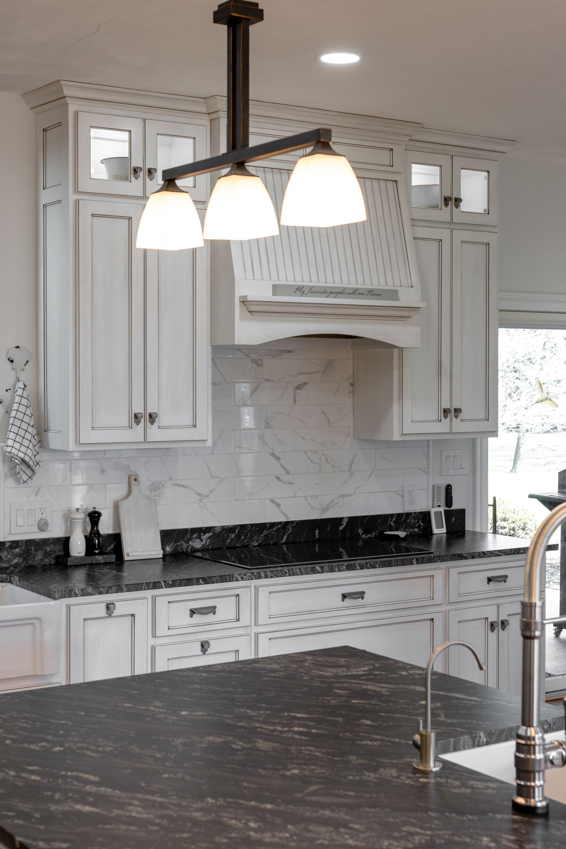 White kitchen with black countertops and a three-light pendant.