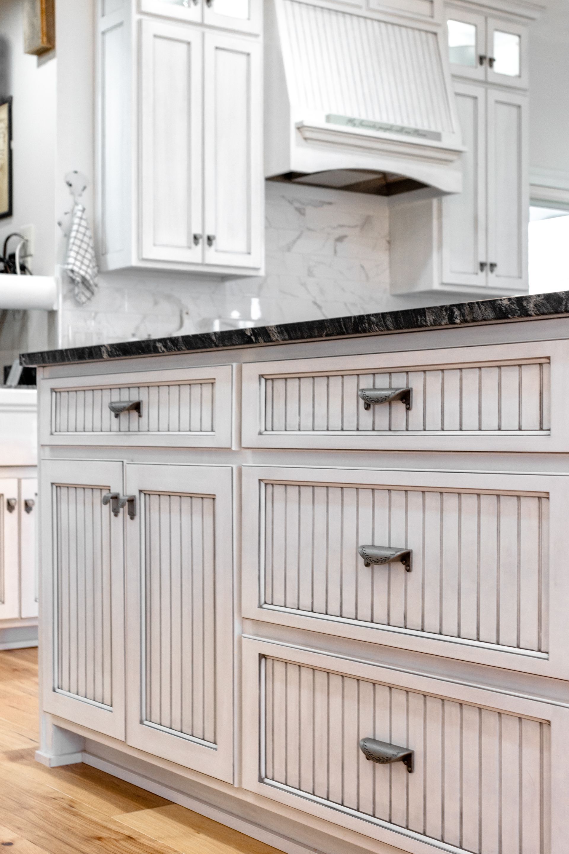 White kitchen island with vertical grooved paneling, dark countertop, and silver hardware.
