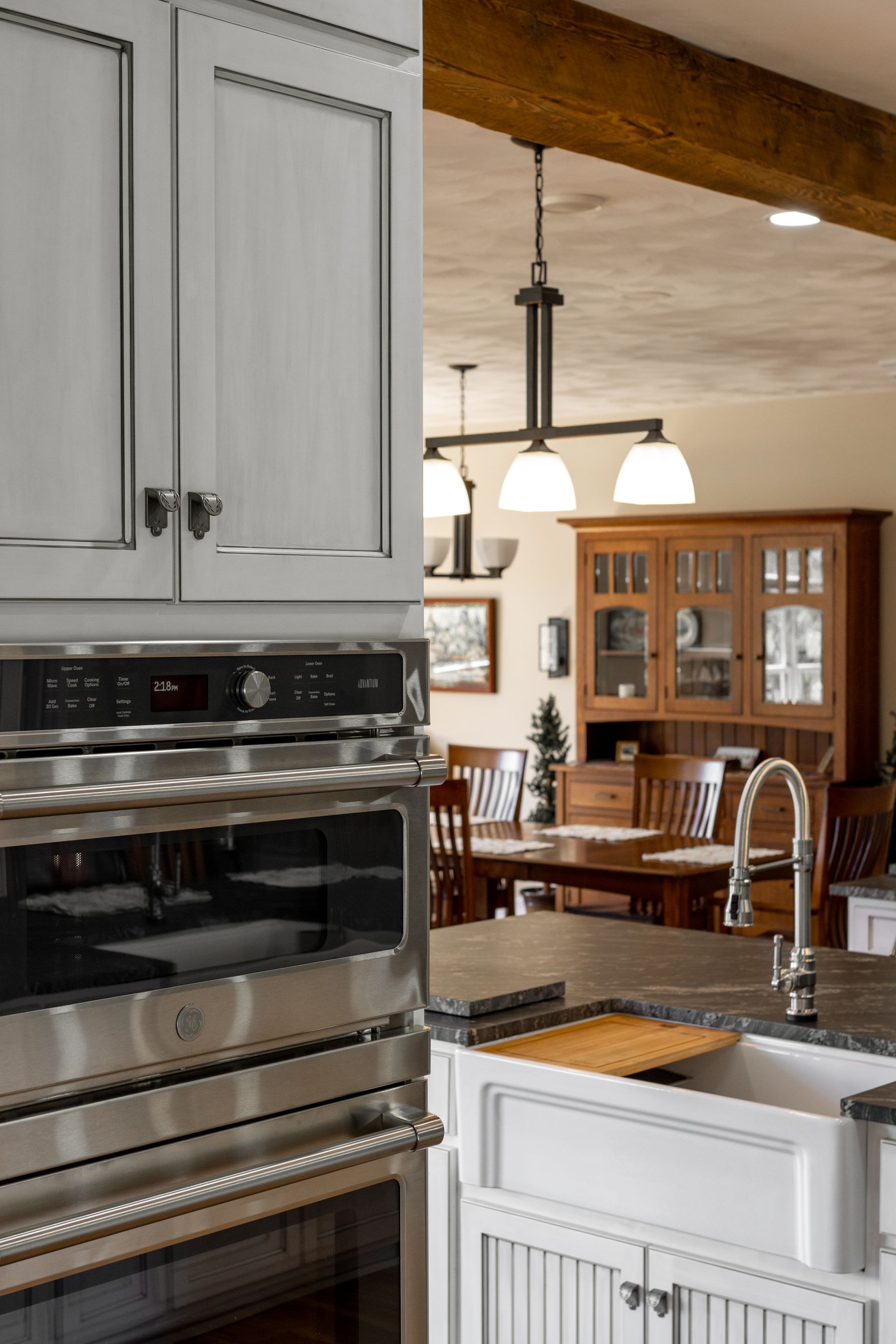 Kitchen with light gray cabinets, stainless steel oven, and view into dining room with wooden furniture.
