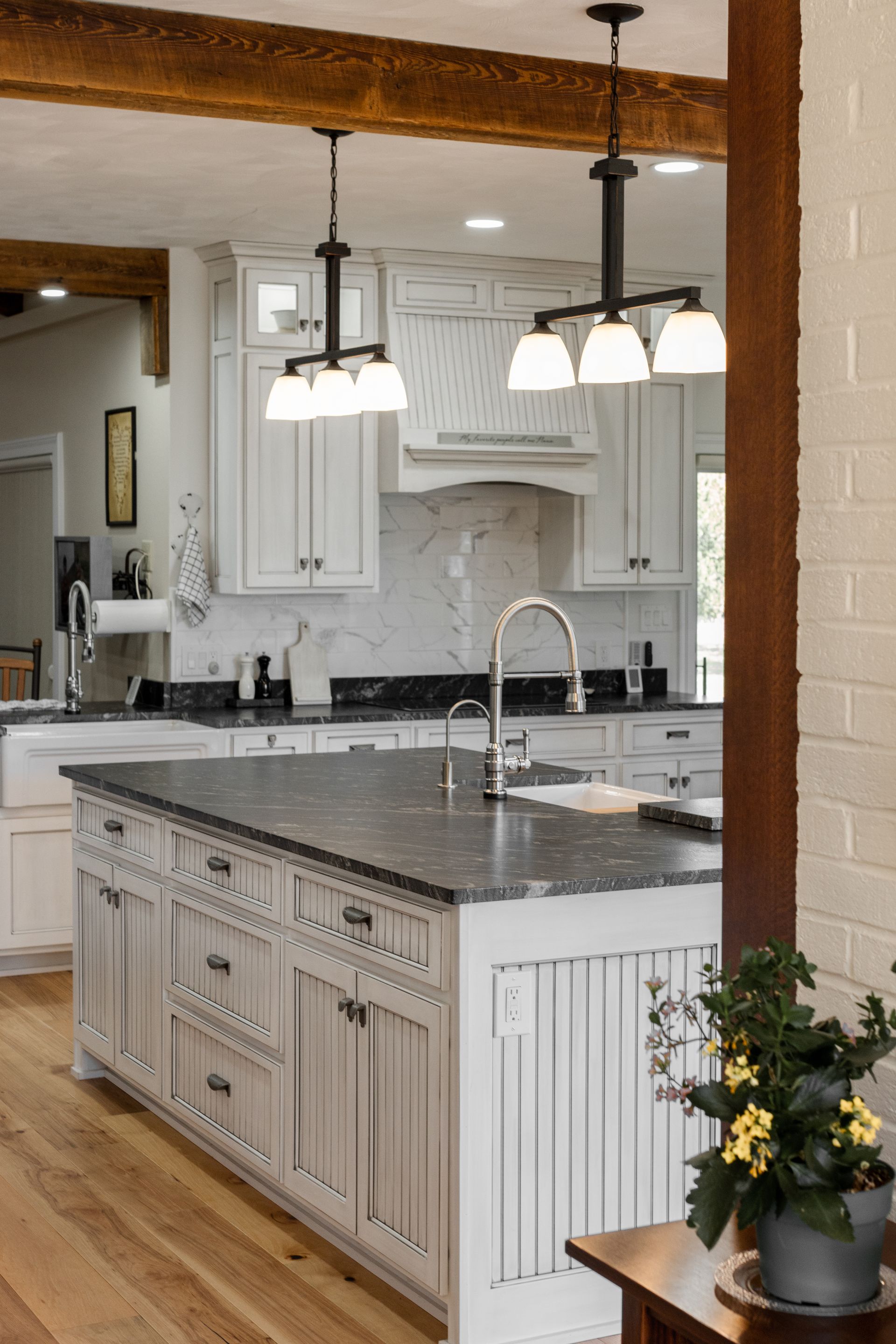 Kitchen with white cabinets, dark island countertop, two pendant lights, and wood beams.