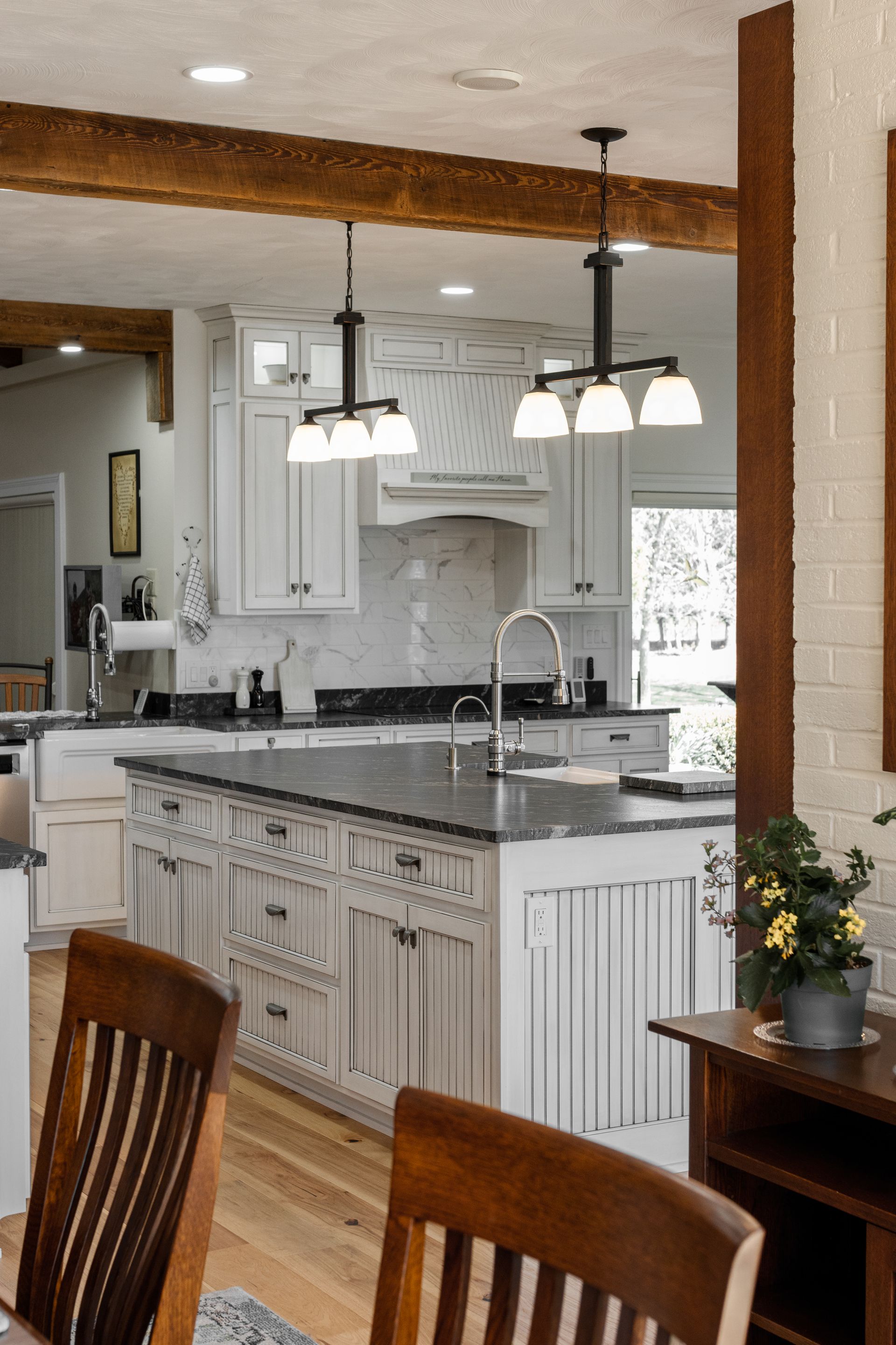 Open kitchen with light gray cabinetry, dark island countertop, and wood beams.