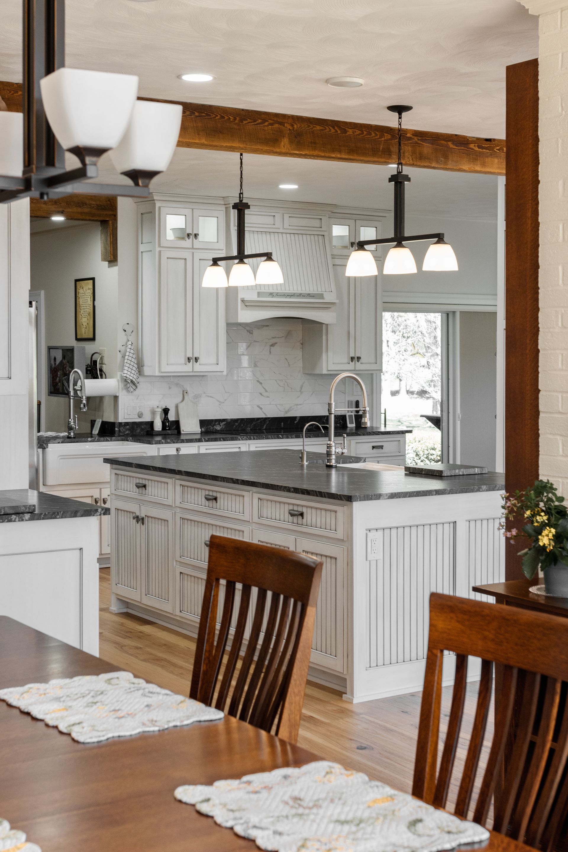 Kitchen with white cabinets, dark countertops, wood beams, and pendant lights.