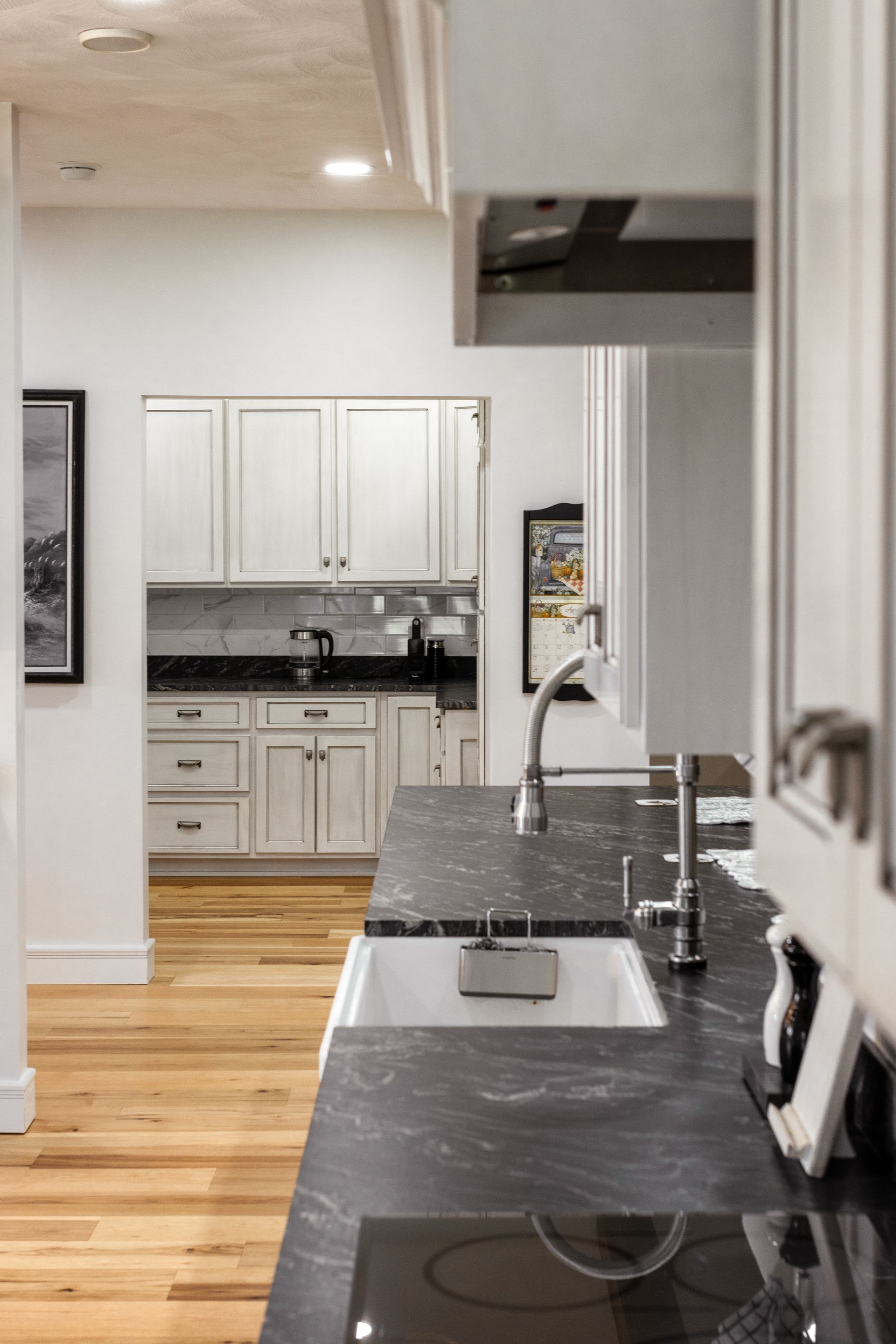 Modern kitchen interior with white cabinets, dark countertops, and wood floors.