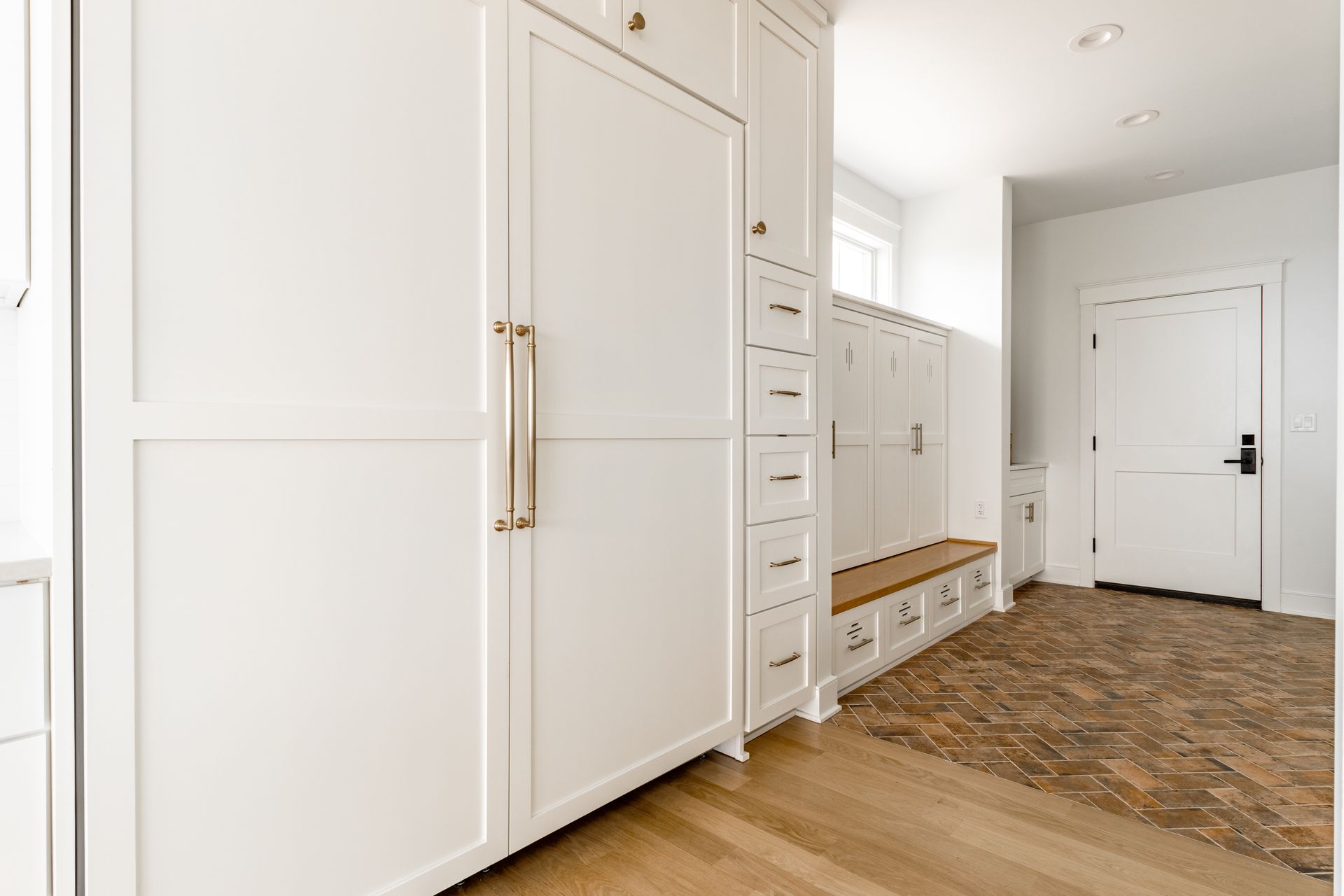 White built-in storage unit with drawers, bench, and door in a hallway with wood flooring.