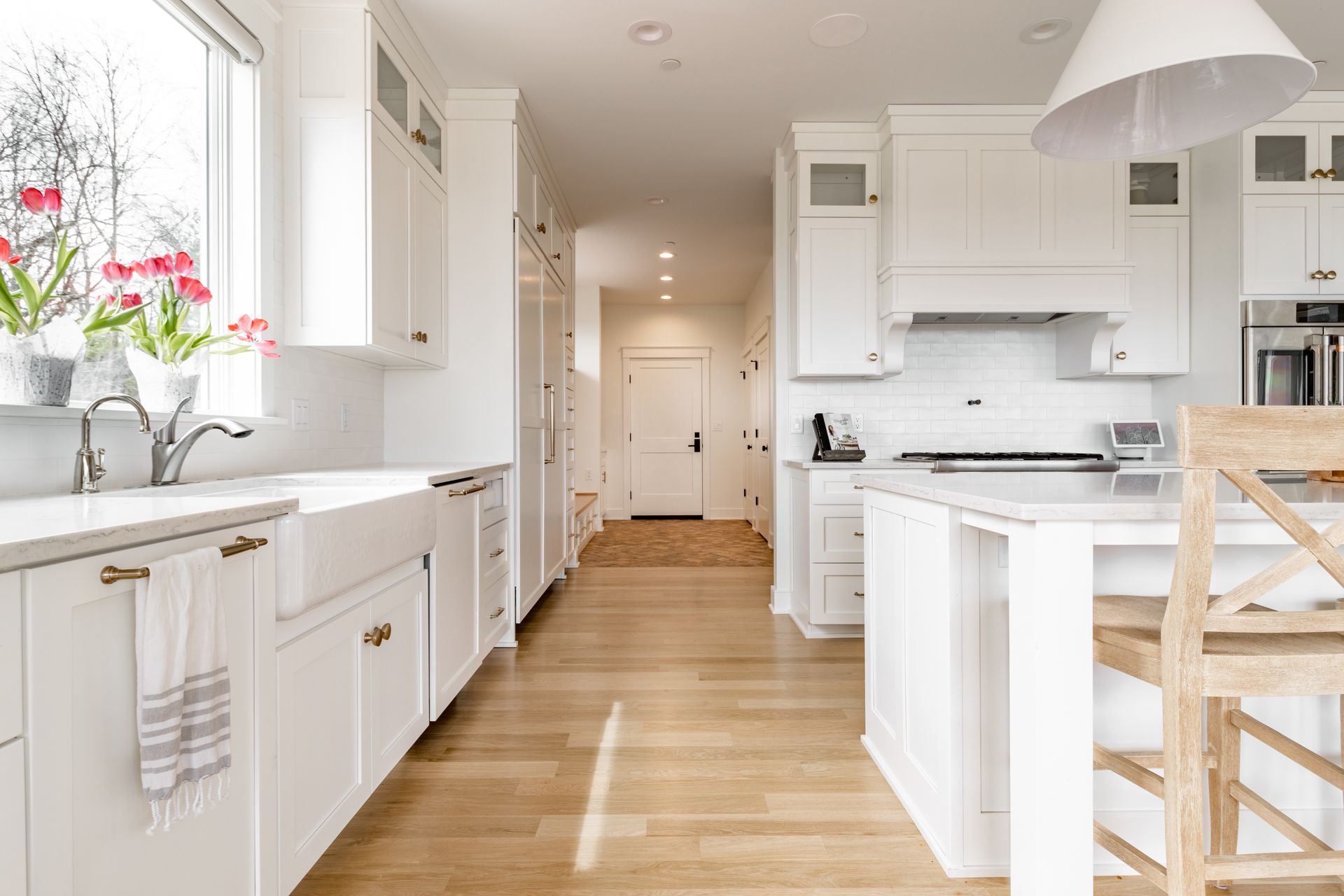 Bright white kitchen with wooden floors, cabinets, and a farmhouse sink.