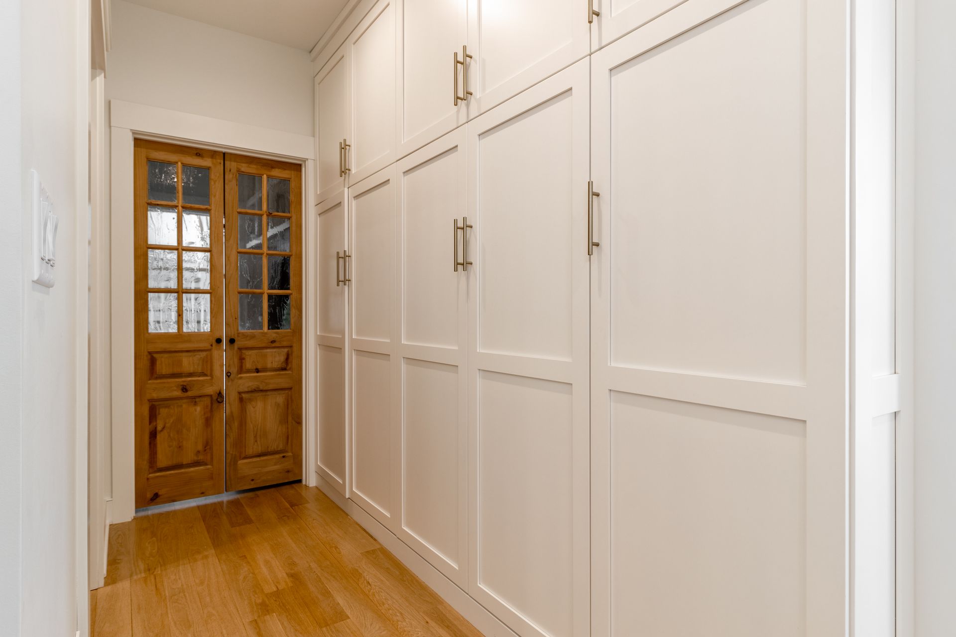 Hallway with white storage cabinets and wood doors.