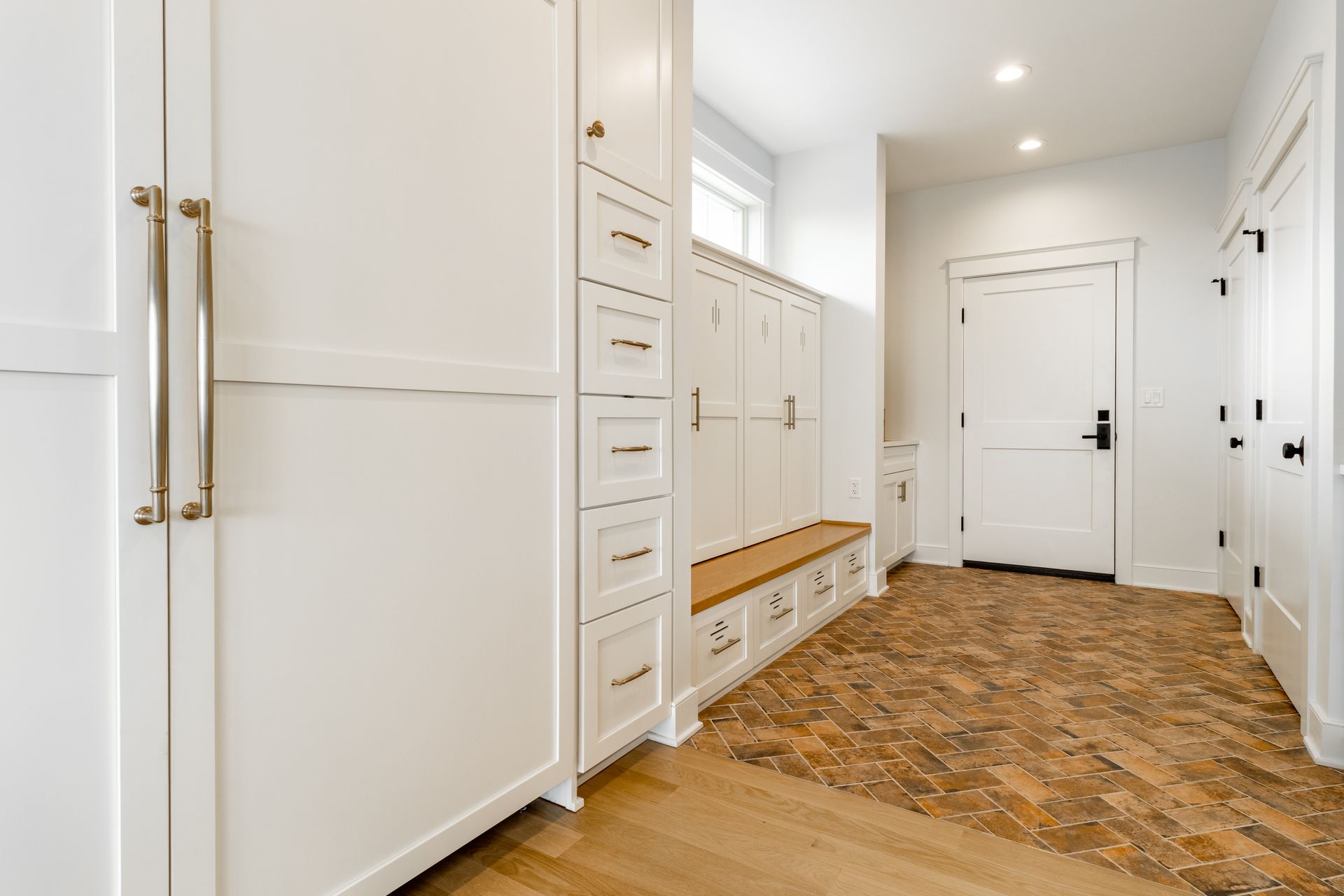 White hallway with built-in storage cabinets, a wooden bench, and a door, featuring light-colored flooring.
