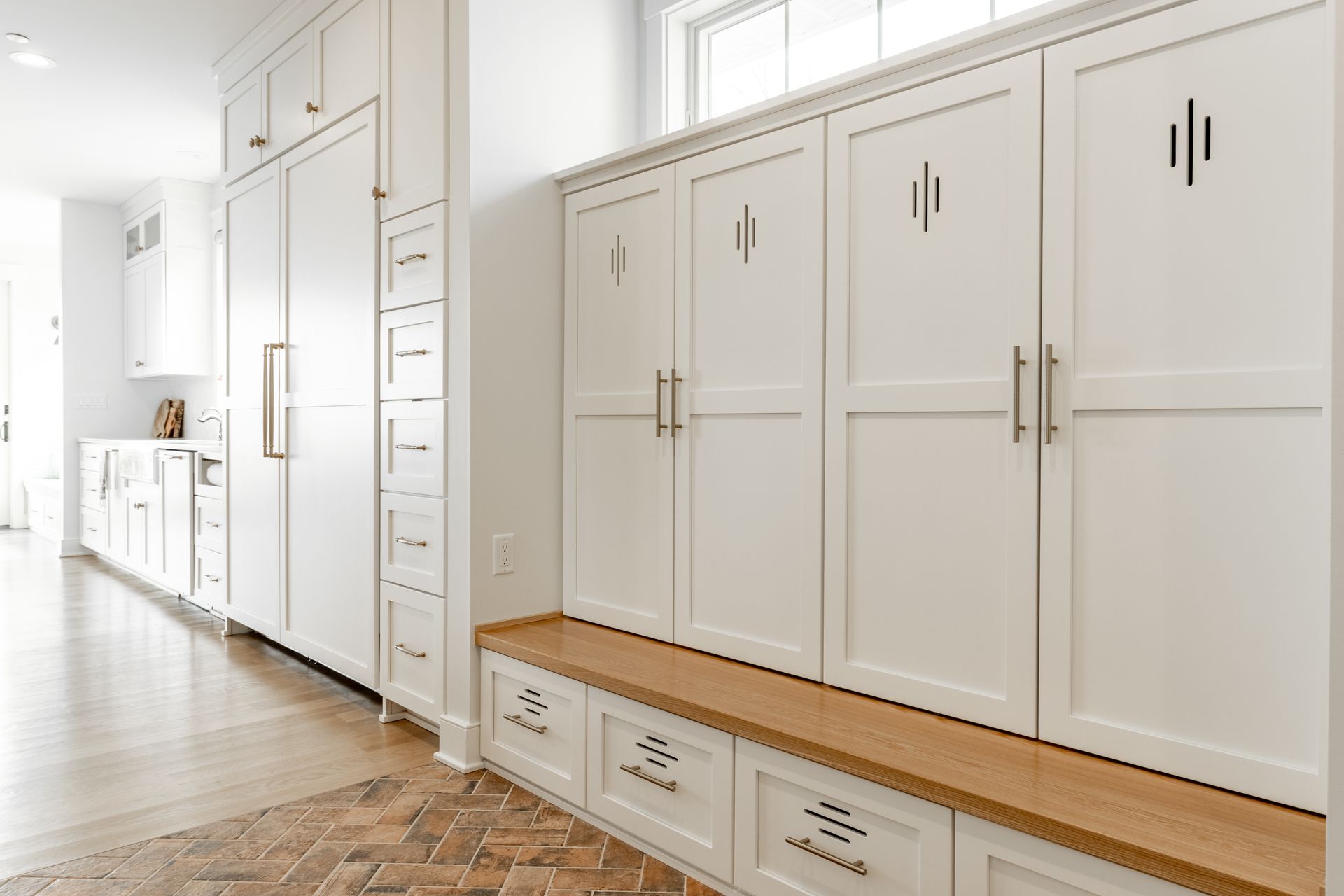 White built-in storage cabinets with wooden accents and handles, a bench, and a brick-patterned floor.