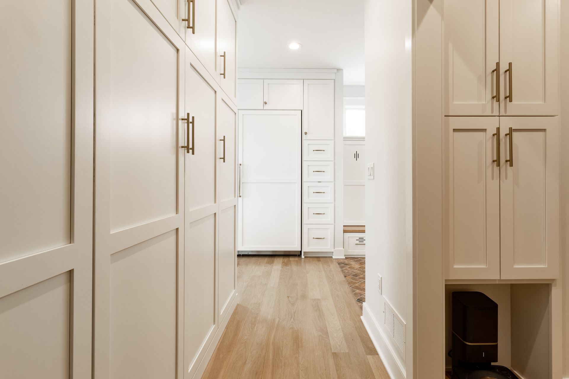 White cabinetry-lined hallway with wood flooring; refrigerator and storage in view.