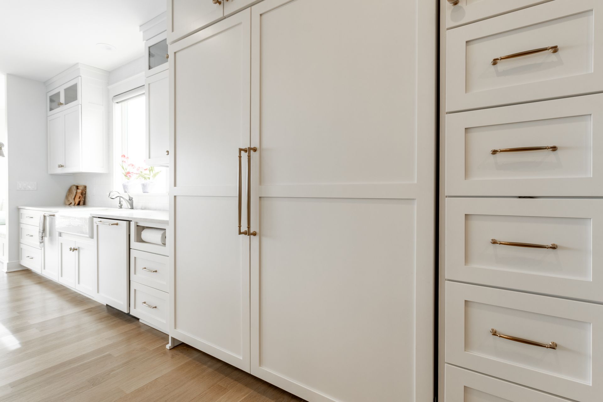 White kitchen with integrated refrigerator and cabinets, gold hardware, light wood floor.