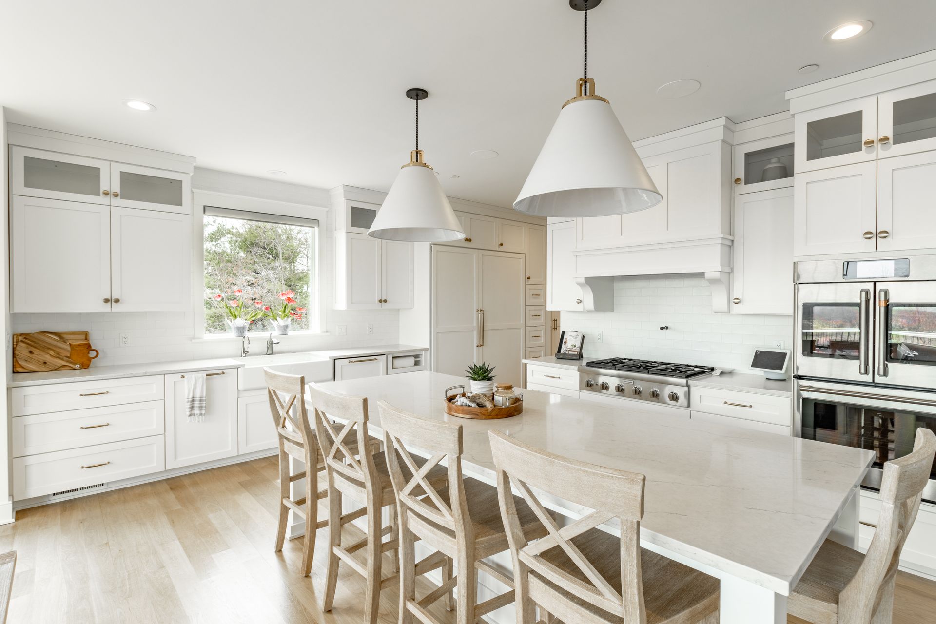 White kitchen with a large island, pendant lights, and wooden chairs.