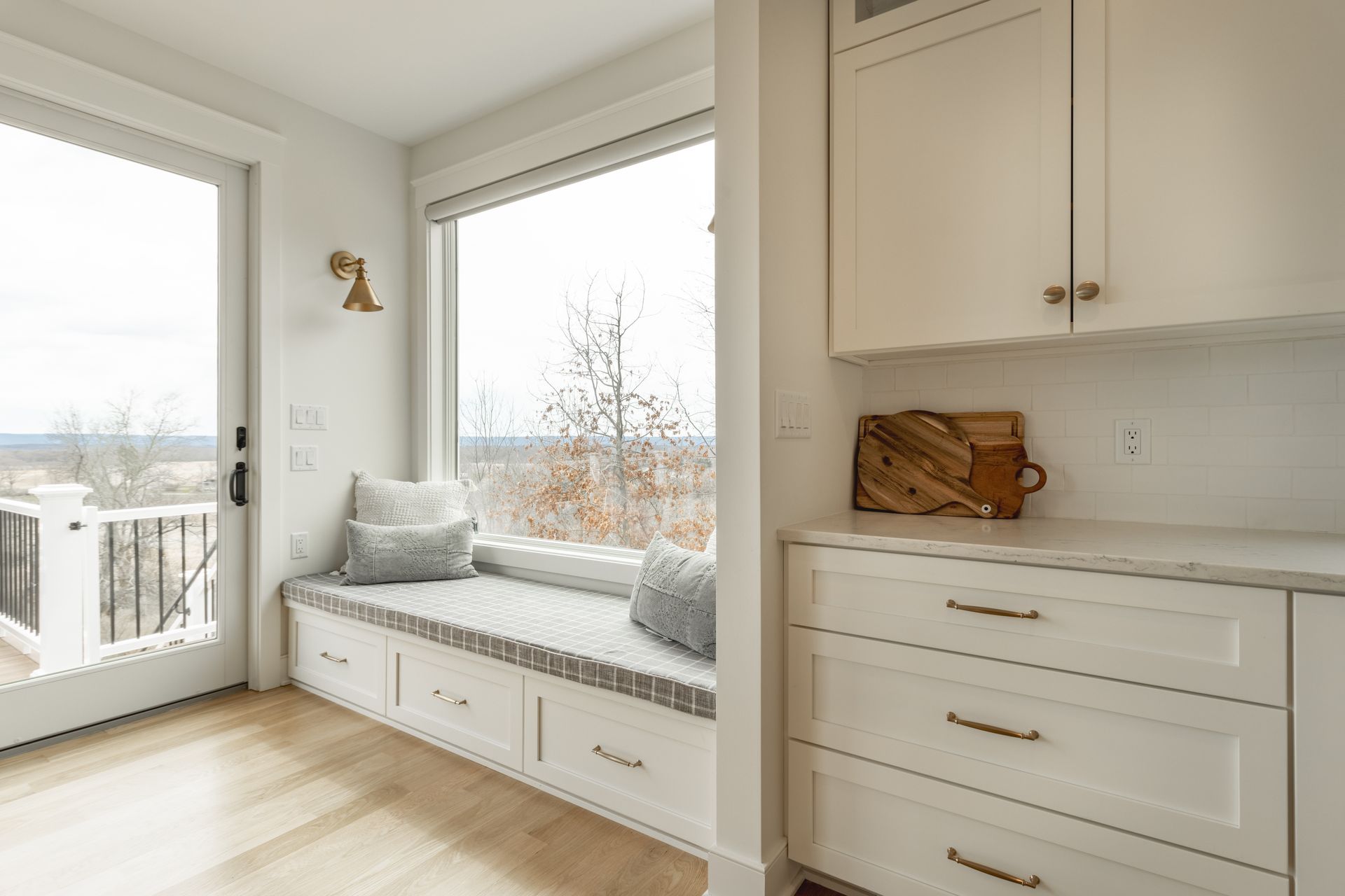 Window seat with built-in drawers, overlooking a landscape. White cabinetry and light wood floors.