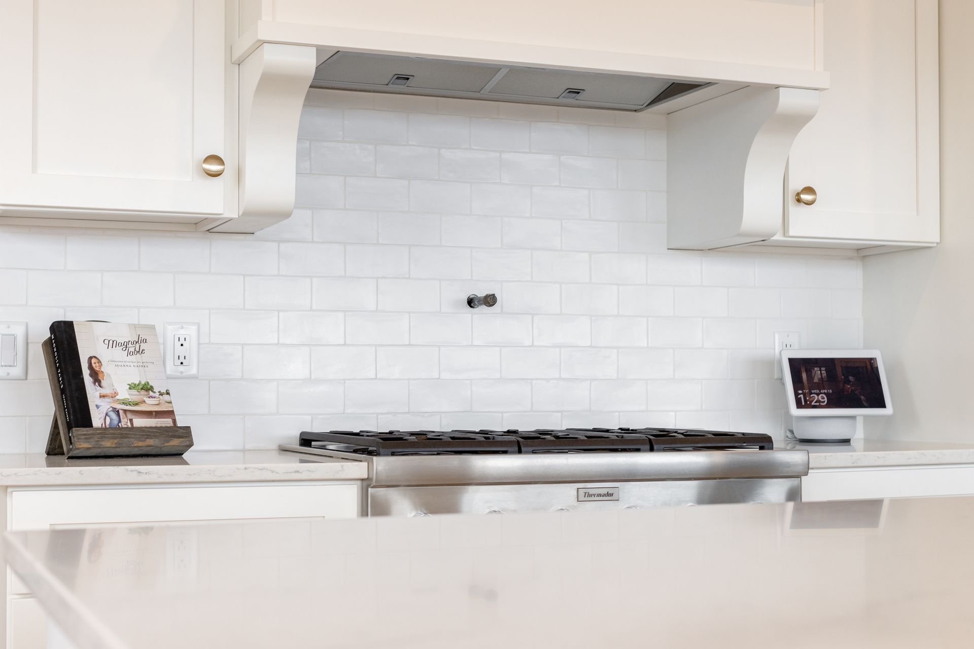 White kitchen with range, backsplash, cabinets, and cookbook. An electronic tablet sits on counter.