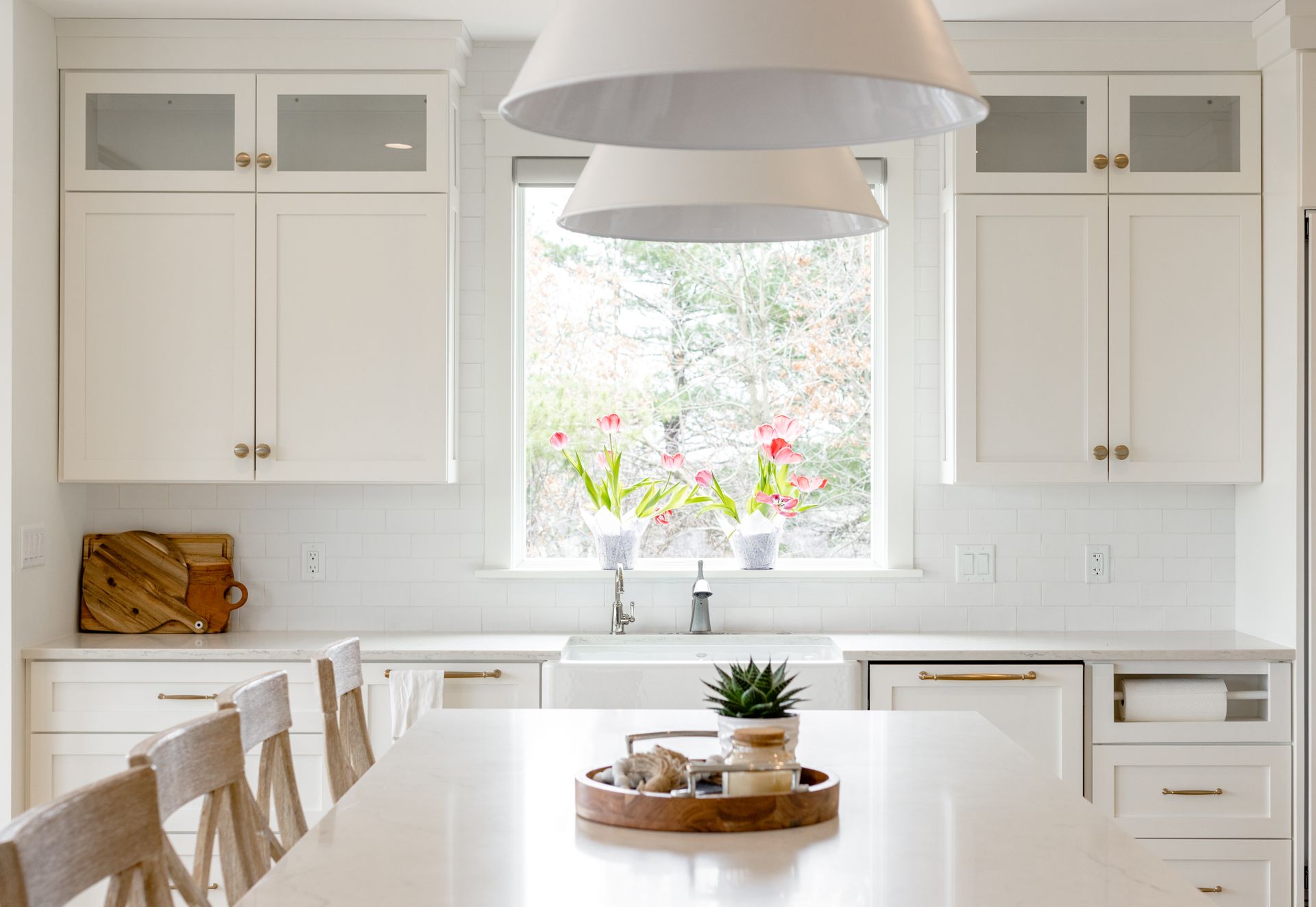 White kitchen with island, cabinets, window, and pendant lights.
