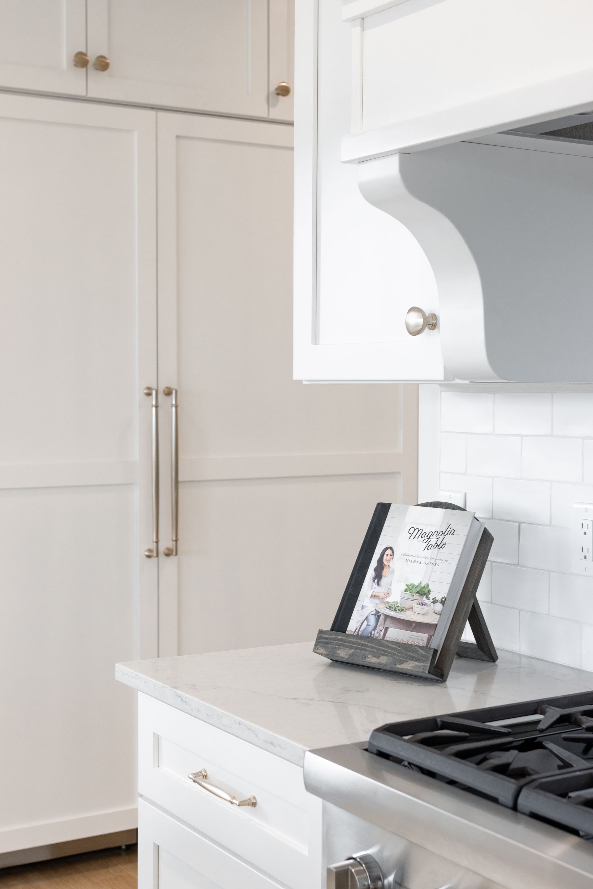 White kitchen with cookbook on counter. Stainless steel stove and cabinets.