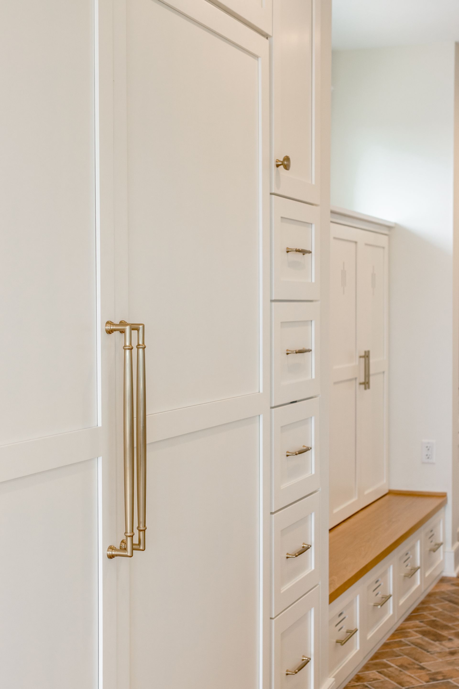 White built-in storage unit with brass hardware. Includes drawers, cabinets, and a bench with wood seat.