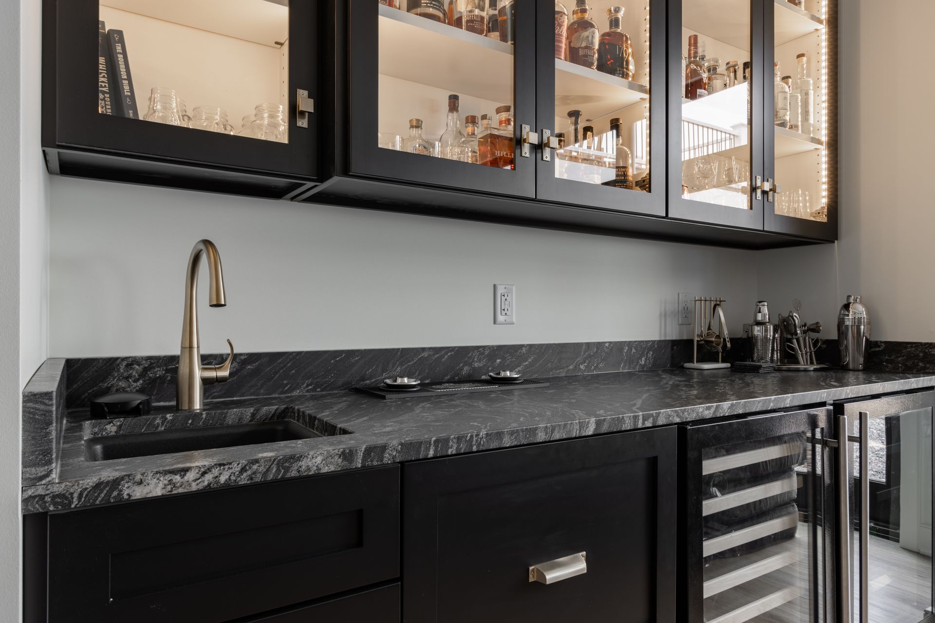 Dark bar with liquor cabinets, a sink, a wine fridge, and a black countertop.