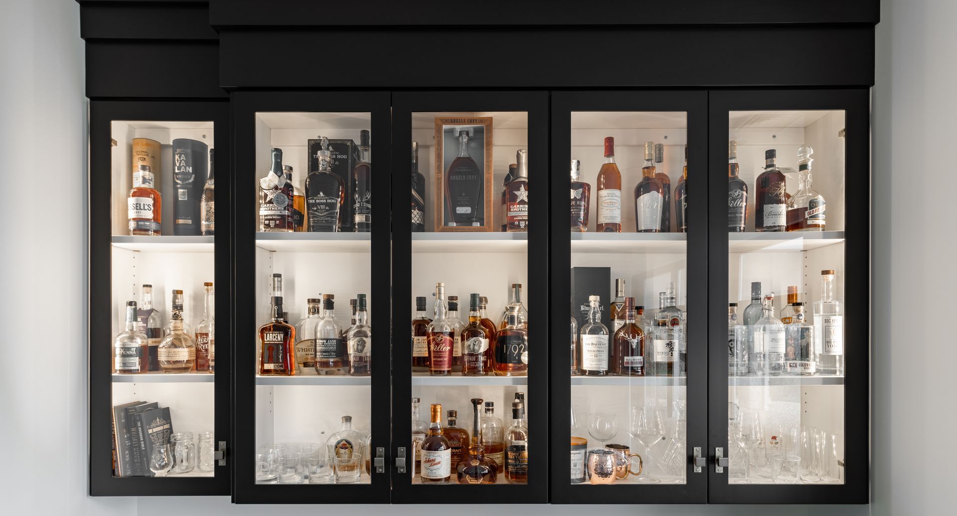 Black liquor cabinet with glass doors, illuminated, filled with various bottles and glasses.
