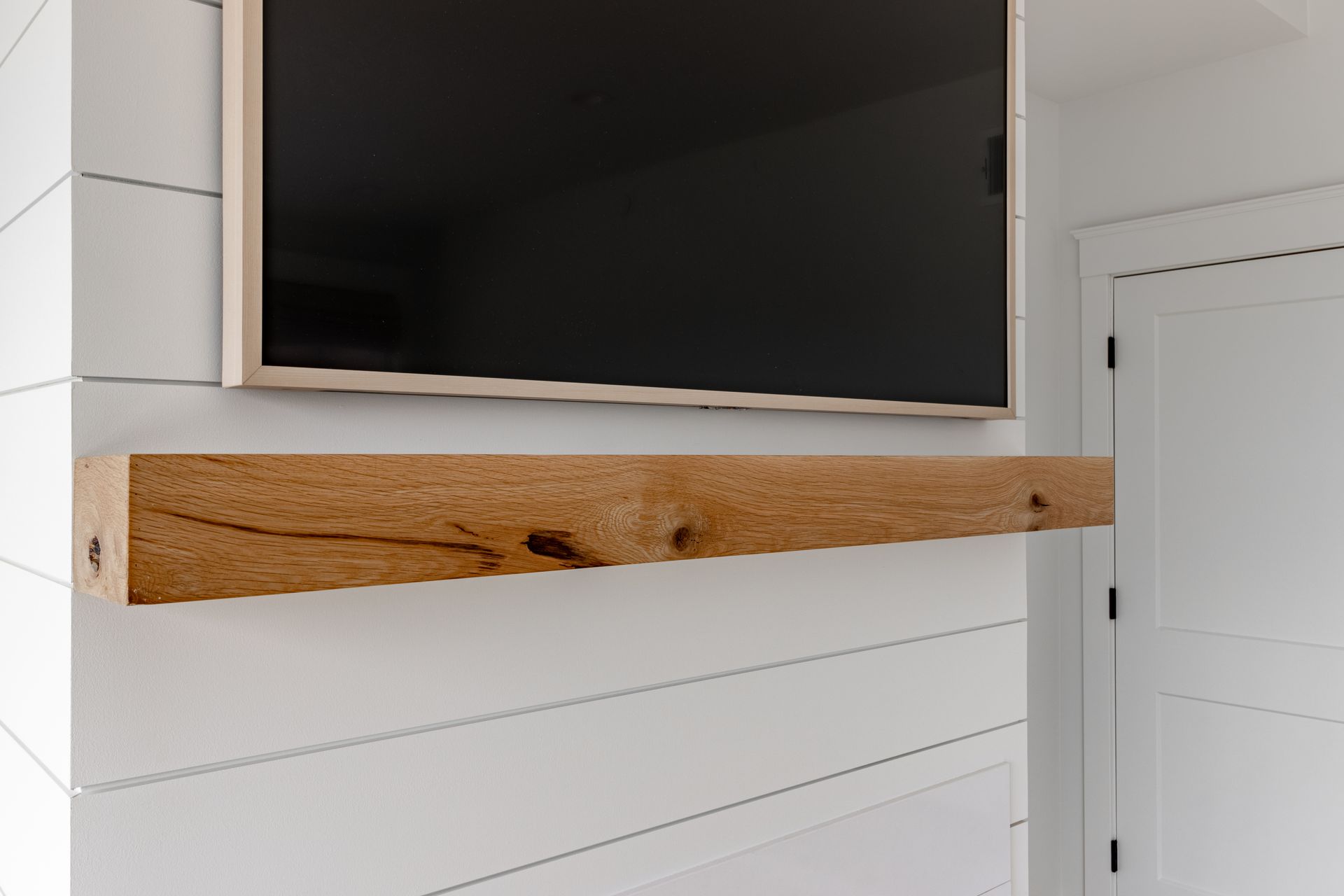 Brown wooden shelf below a mounted television on a white paneled wall.