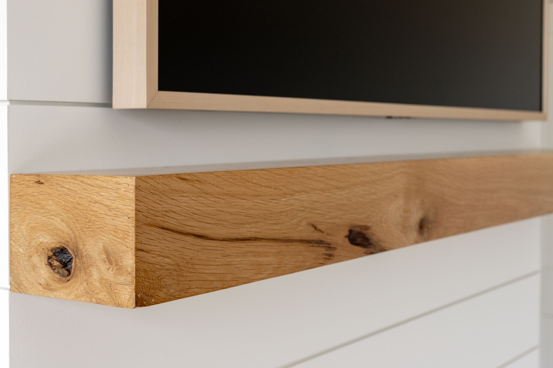 Wooden beam shelf below a mounted black screen on a white shiplap wall.