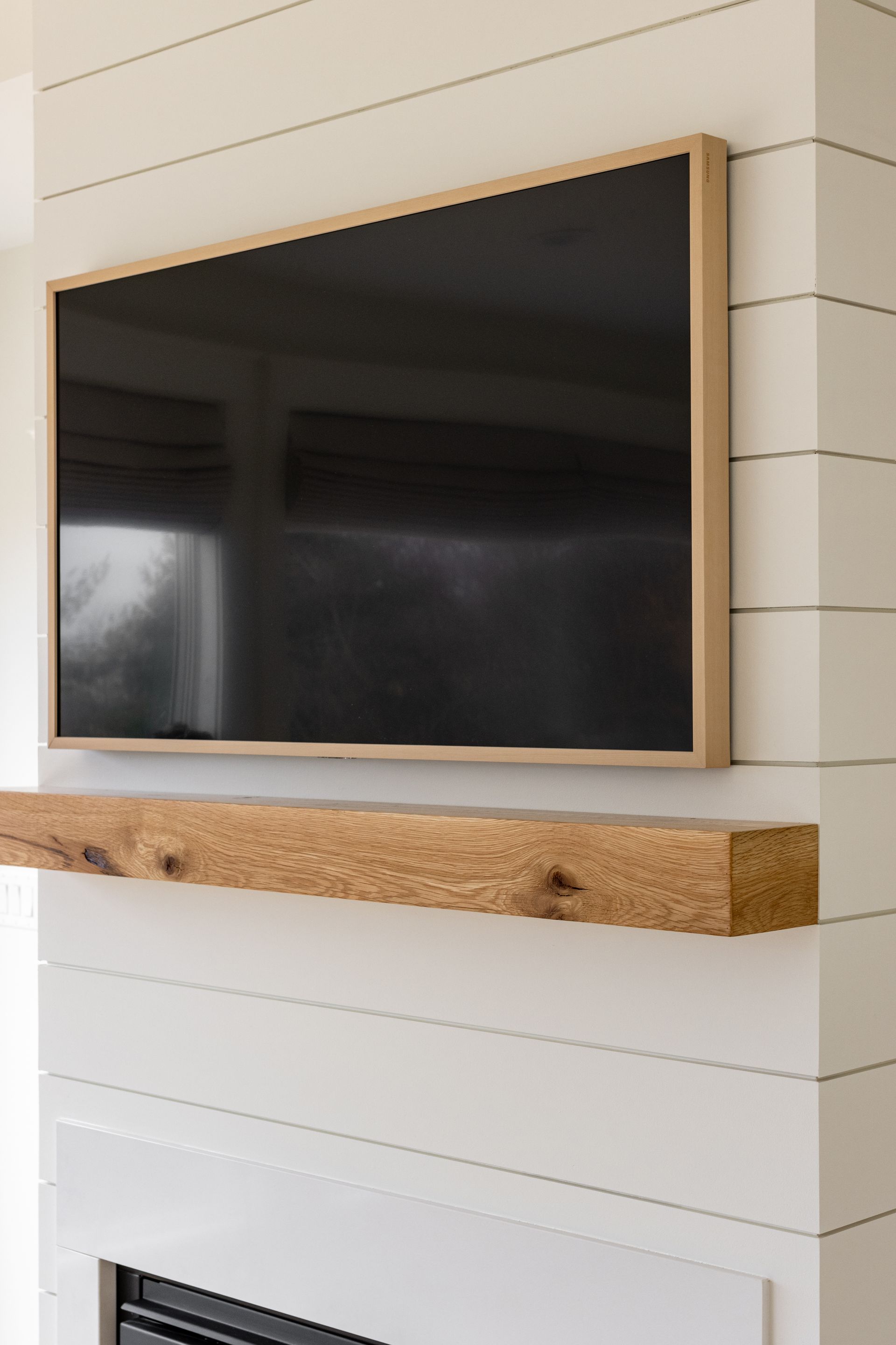 TV mounted above a wooden mantel on a white shiplap wall.