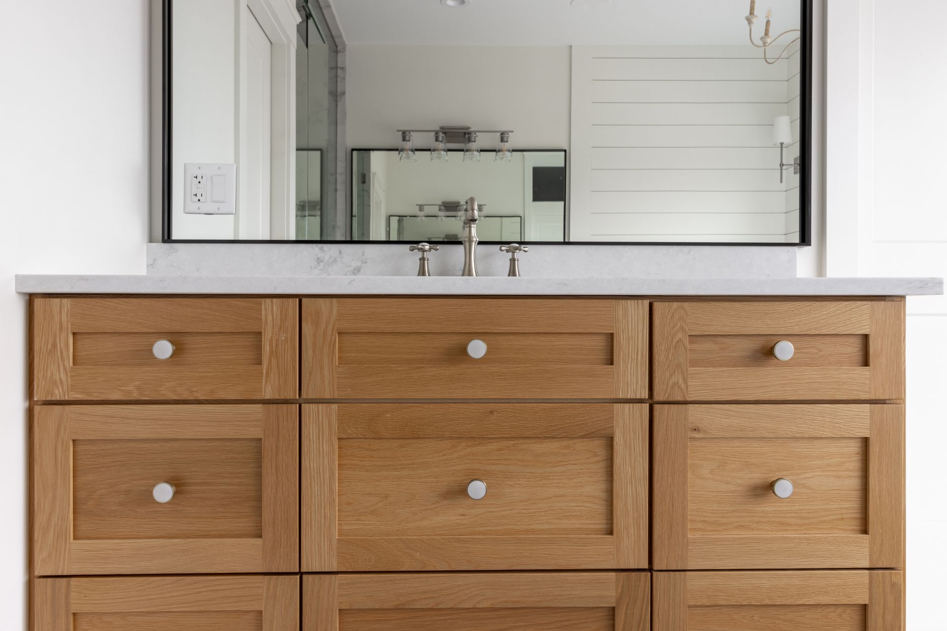 Wooden bathroom vanity with marble top, large mirror, and silver hardware.