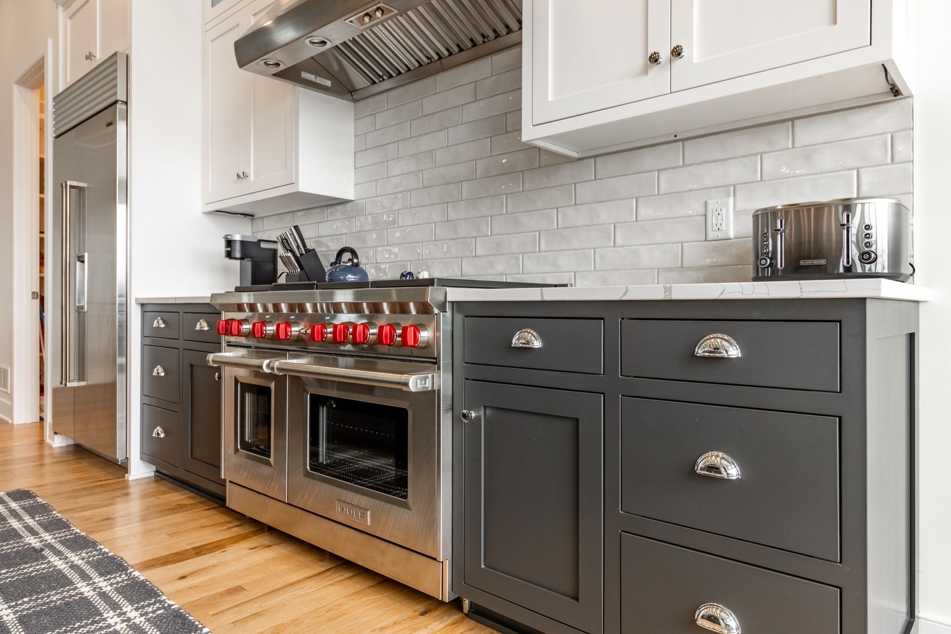 Modern kitchen with stainless steel appliances, dark gray cabinets, white backsplash and wood floors.