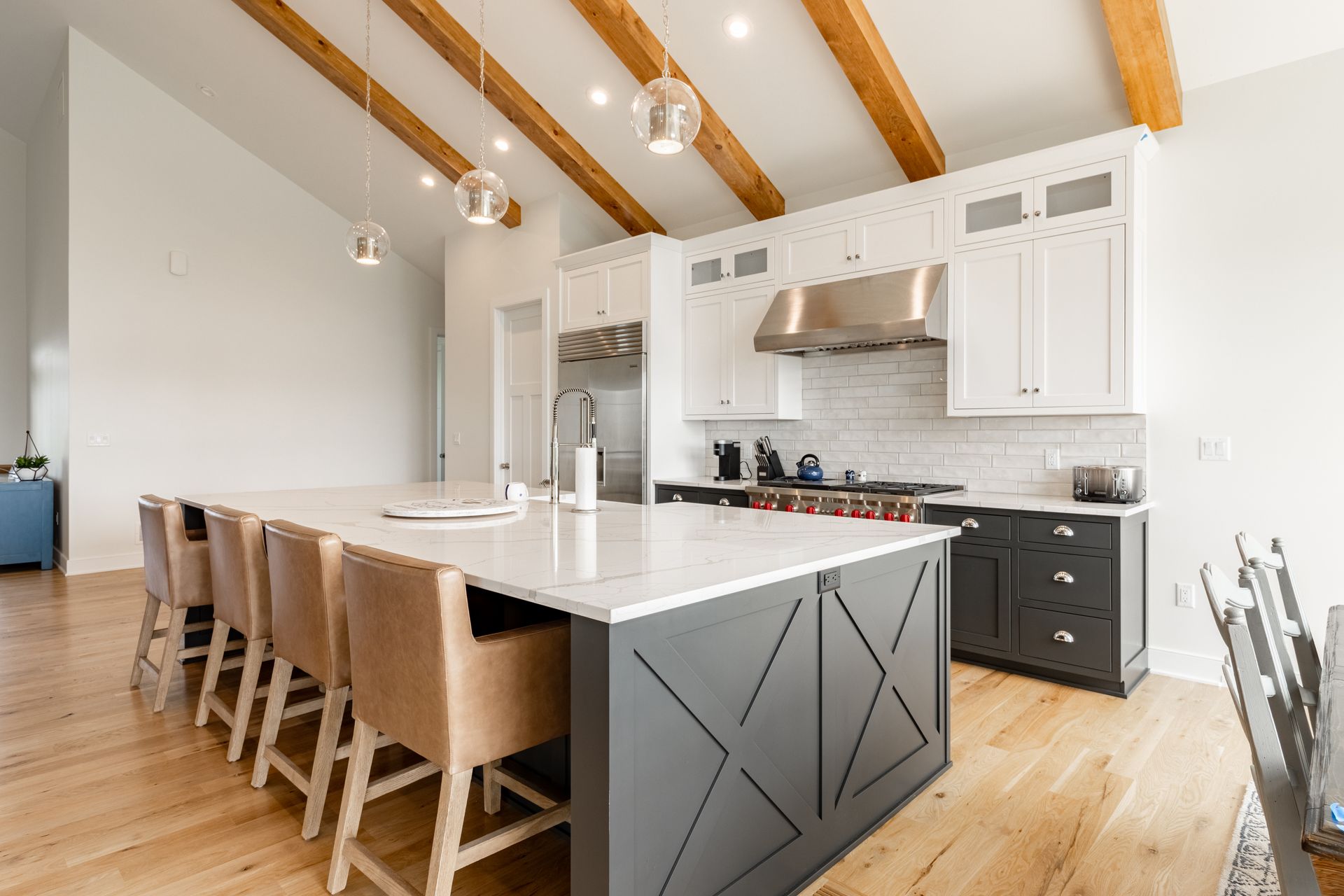 Modern kitchen with large island, white countertops, gray cabinets, wood beams, pendant lights.