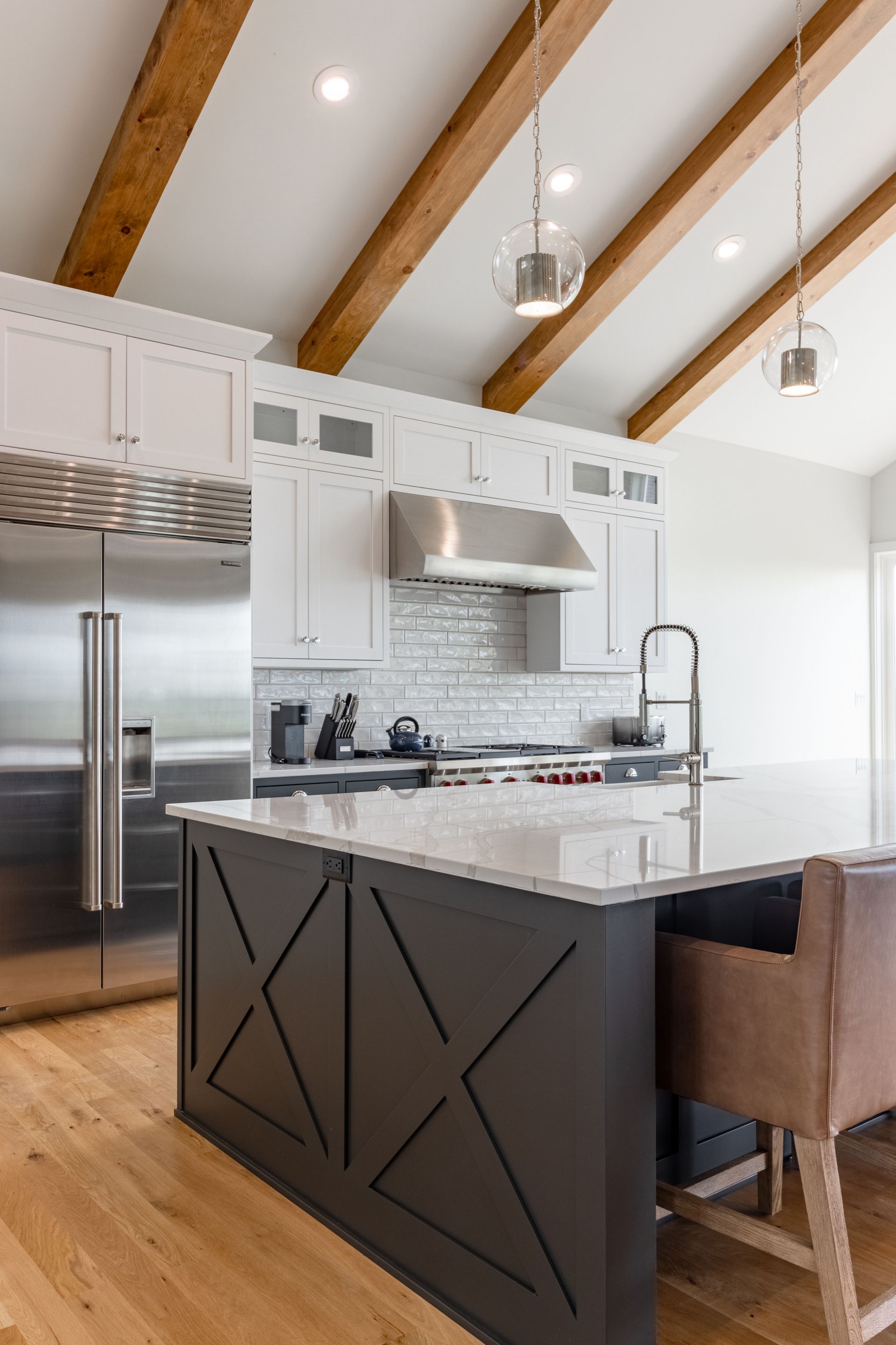 Modern kitchen with gray island, white cabinets, stainless steel appliances, and wood beams.
