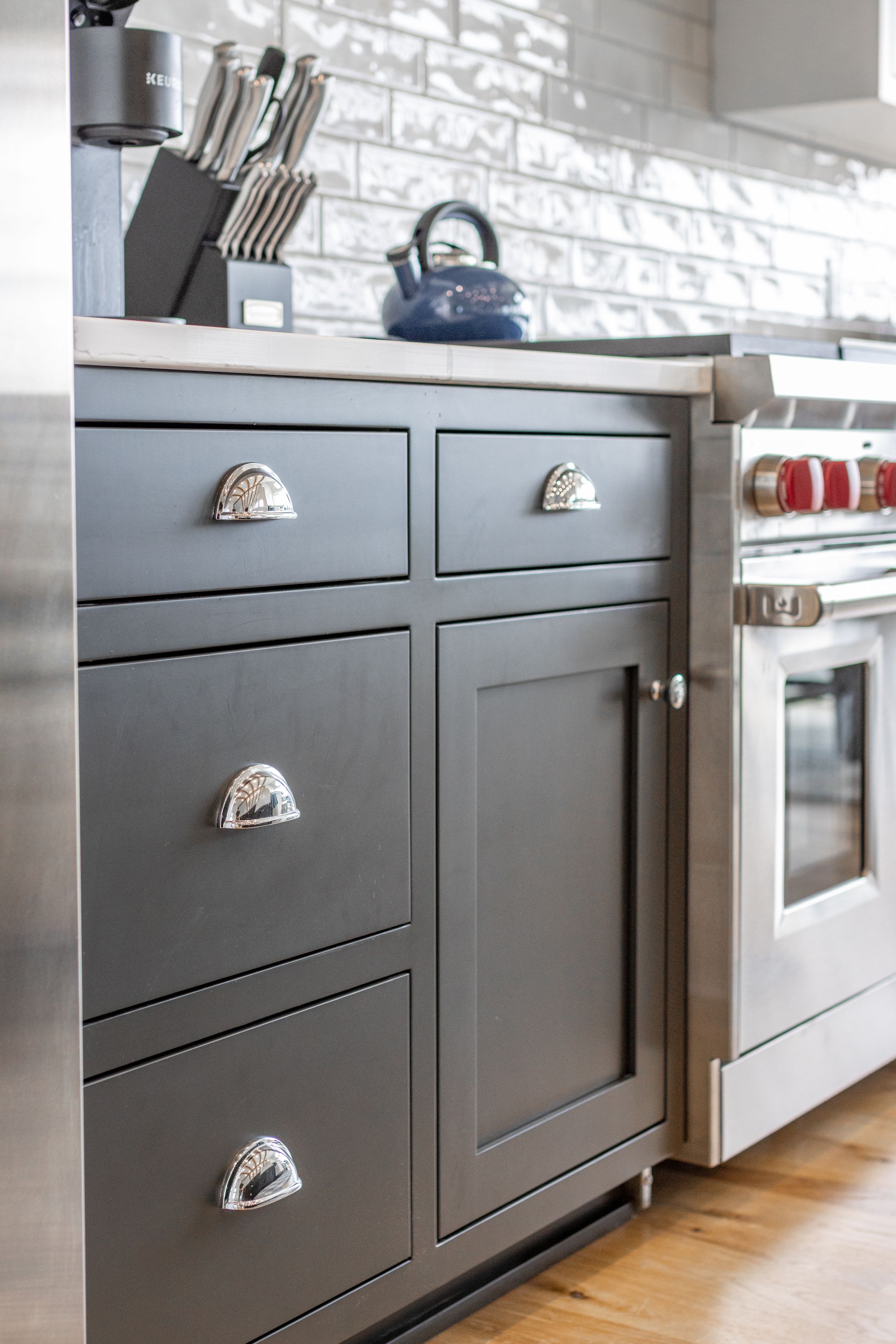 Dark gray kitchen cabinets with silver hardware and a stainless steel range next to them.