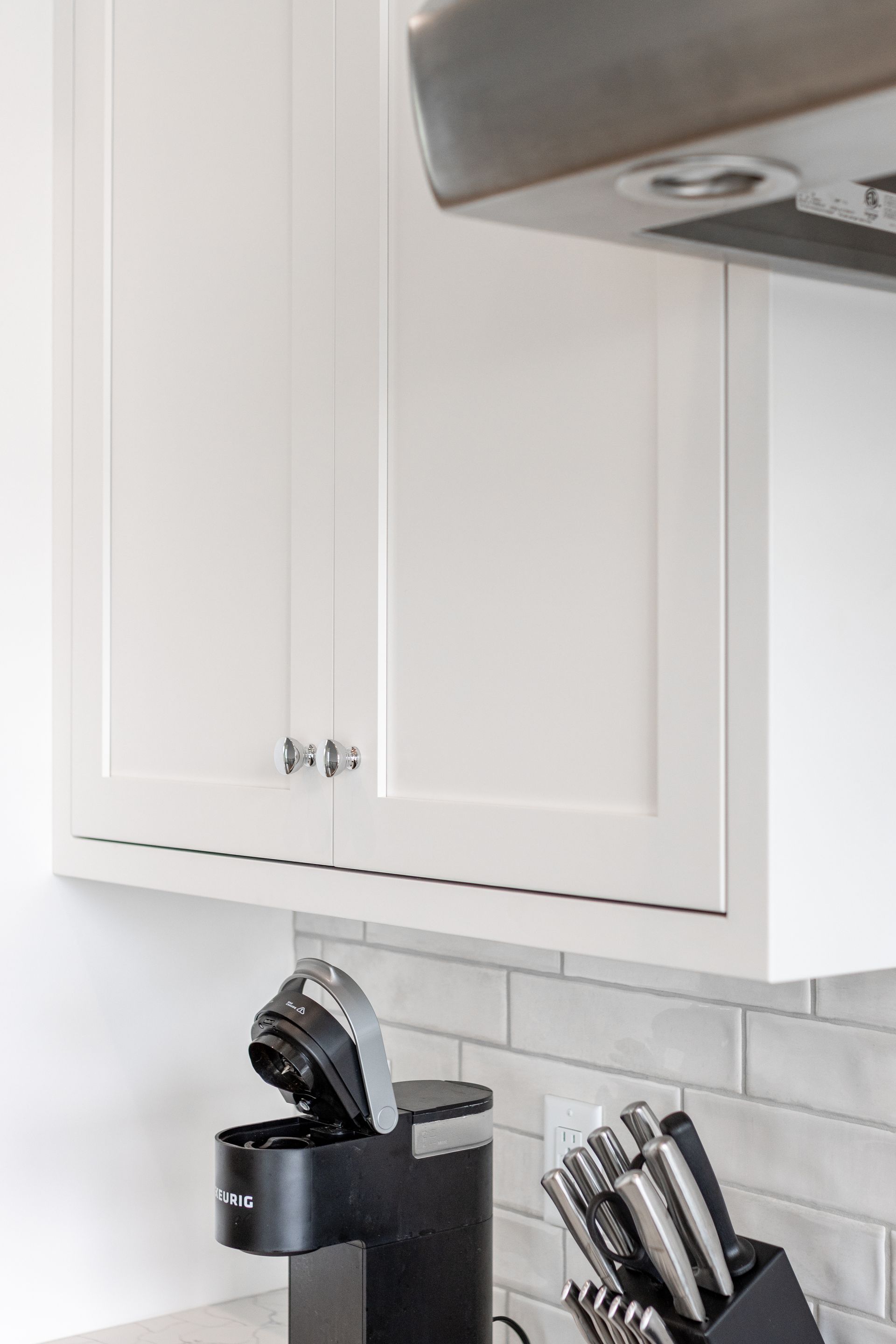 White kitchen cabinets with silver hardware above a coffee maker and a knife block.