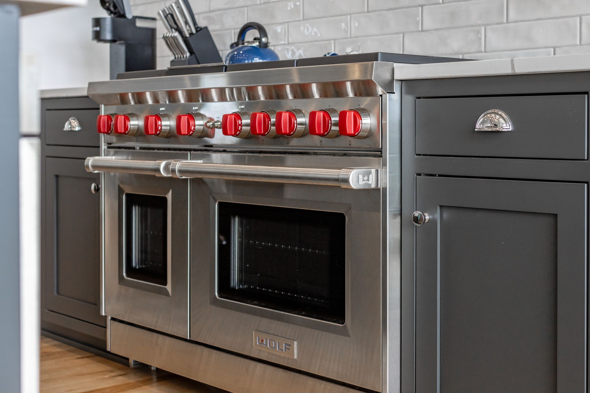 Stainless steel oven with red knobs in a gray kitchen.