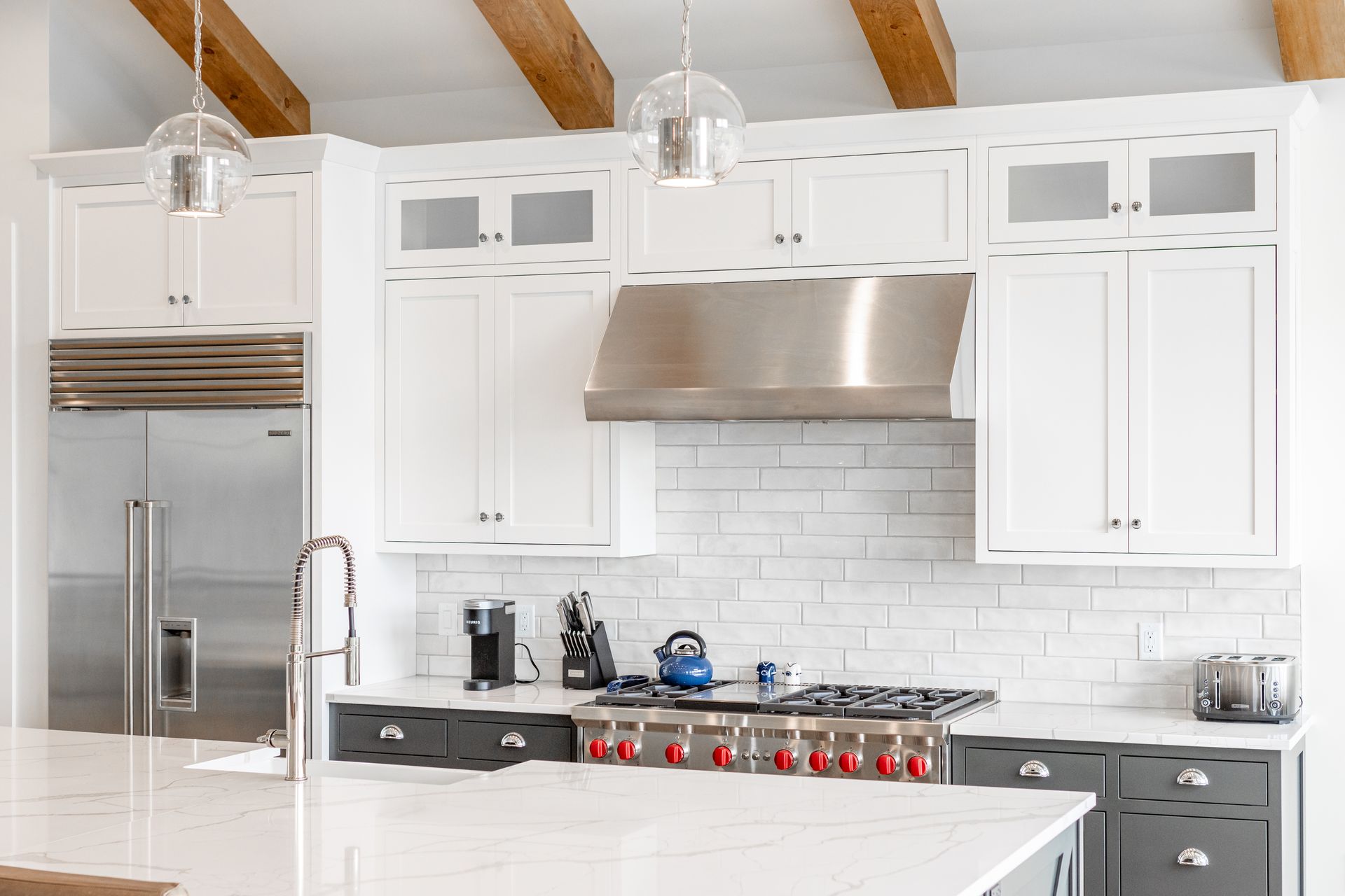 White and gray kitchen with stainless steel appliances, white cabinets, and wooden beams.
