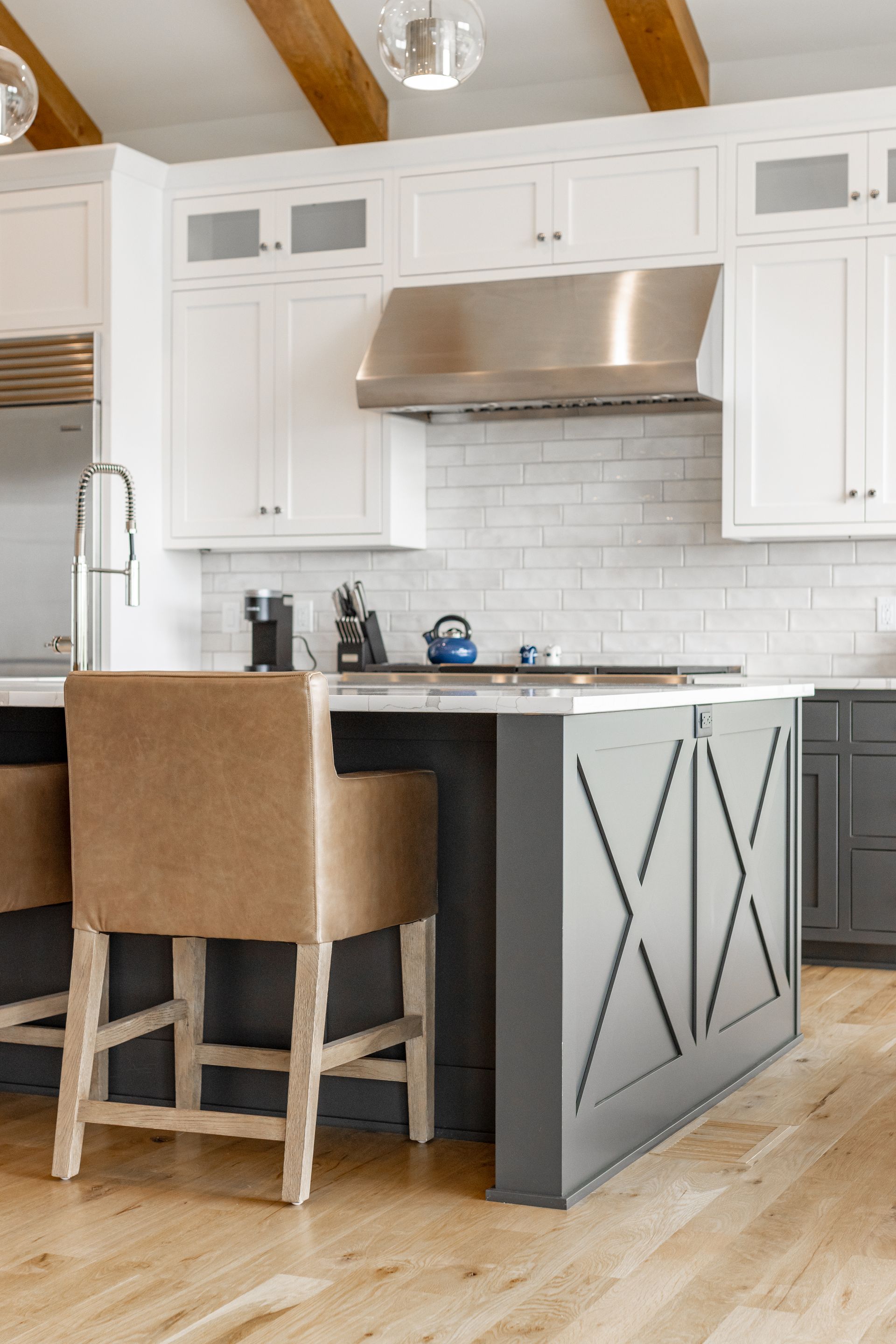 Modern kitchen with white cabinets, gray island, stainless steel range hood, and wooden beams.