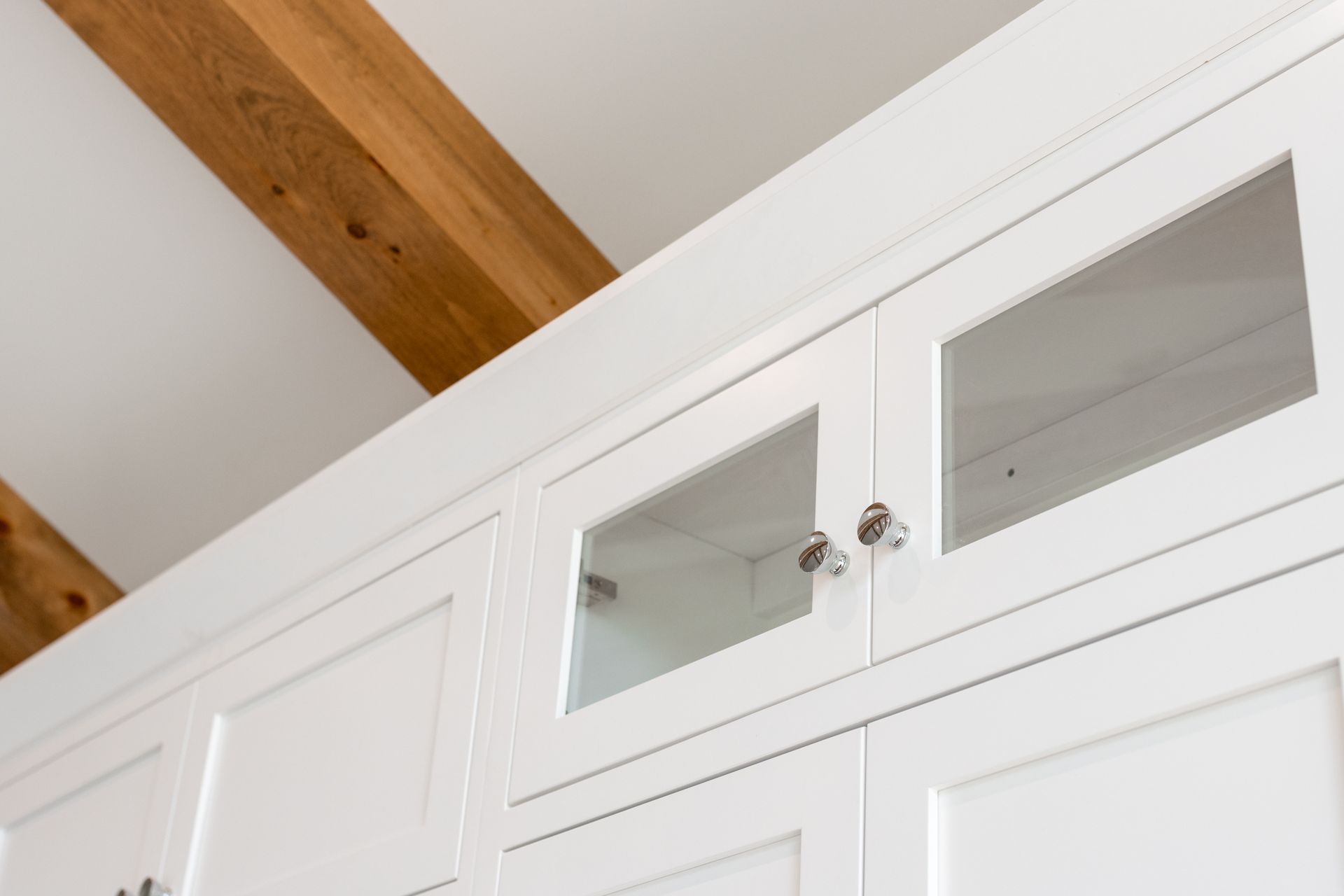 White kitchen cabinets with glass-fronted doors, under a sloped ceiling with exposed wooden beams.