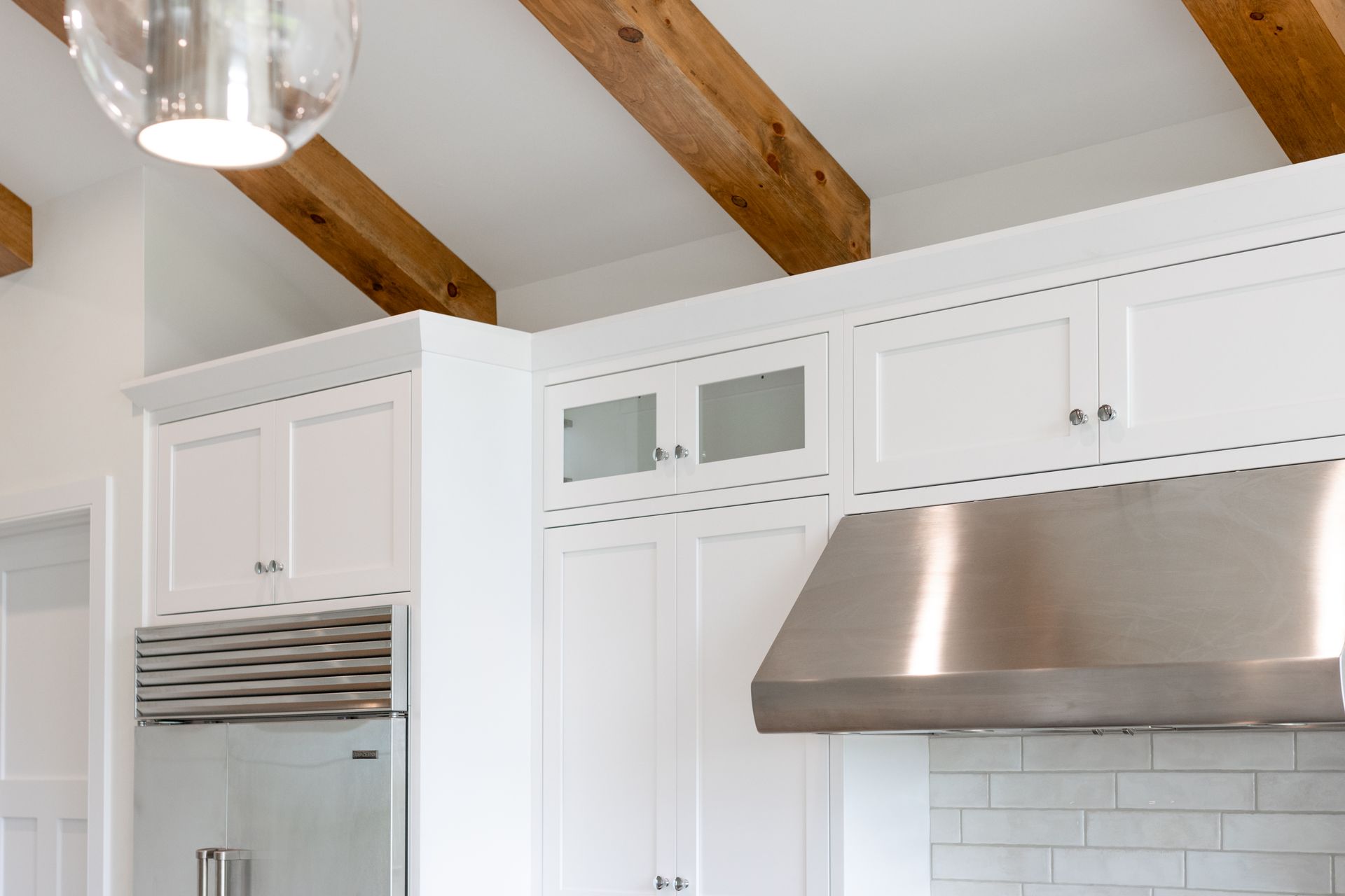 White kitchen cabinets with stainless steel range hood and exposed wooden beams.