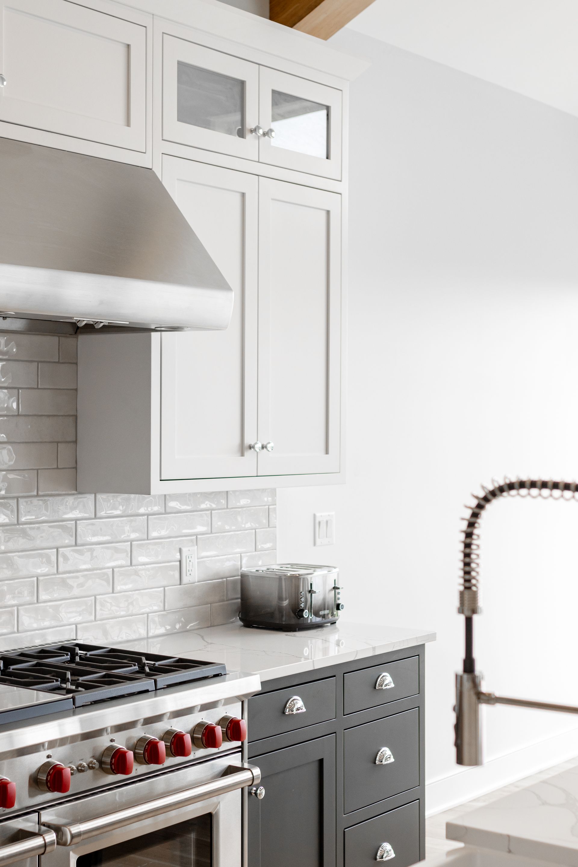 Kitchen with white cabinets, gray lower cabinets, stainless steel stove, and backsplash.