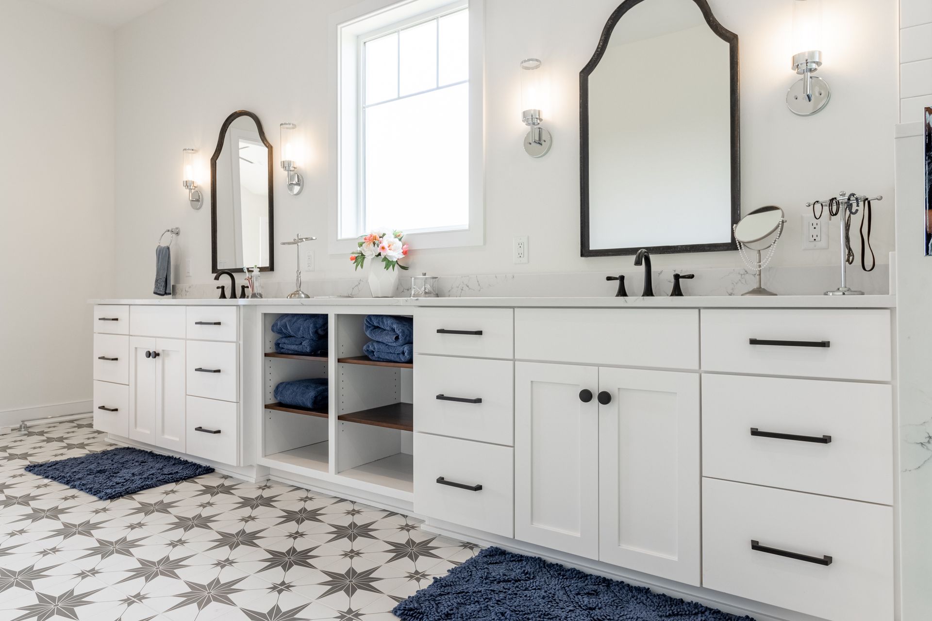 White bathroom with dual sinks, arched mirrors, and patterned floor.